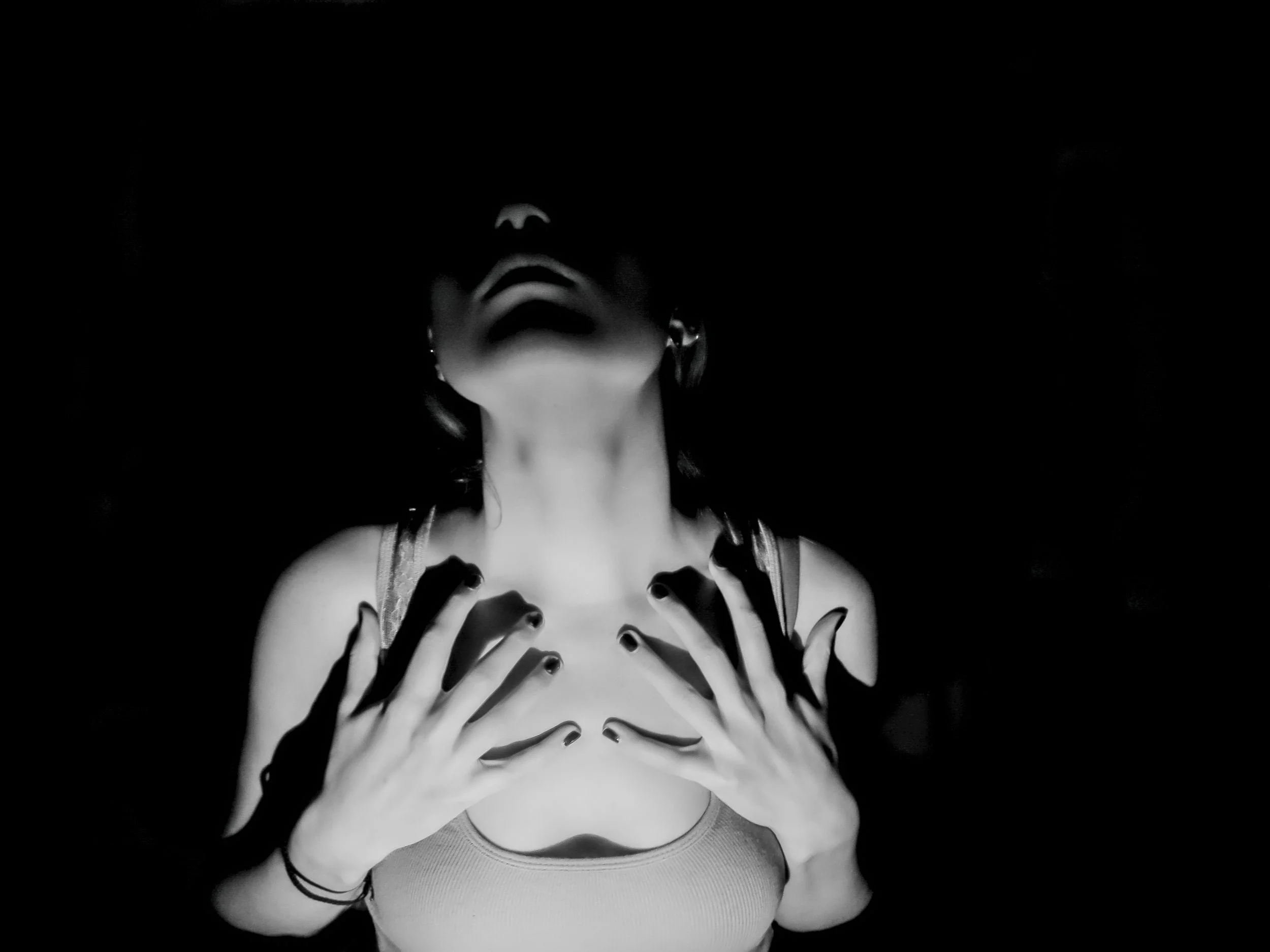 A person with their face obscured by shadows, holding their chest with both hands, in a black and white photo with high contrast.