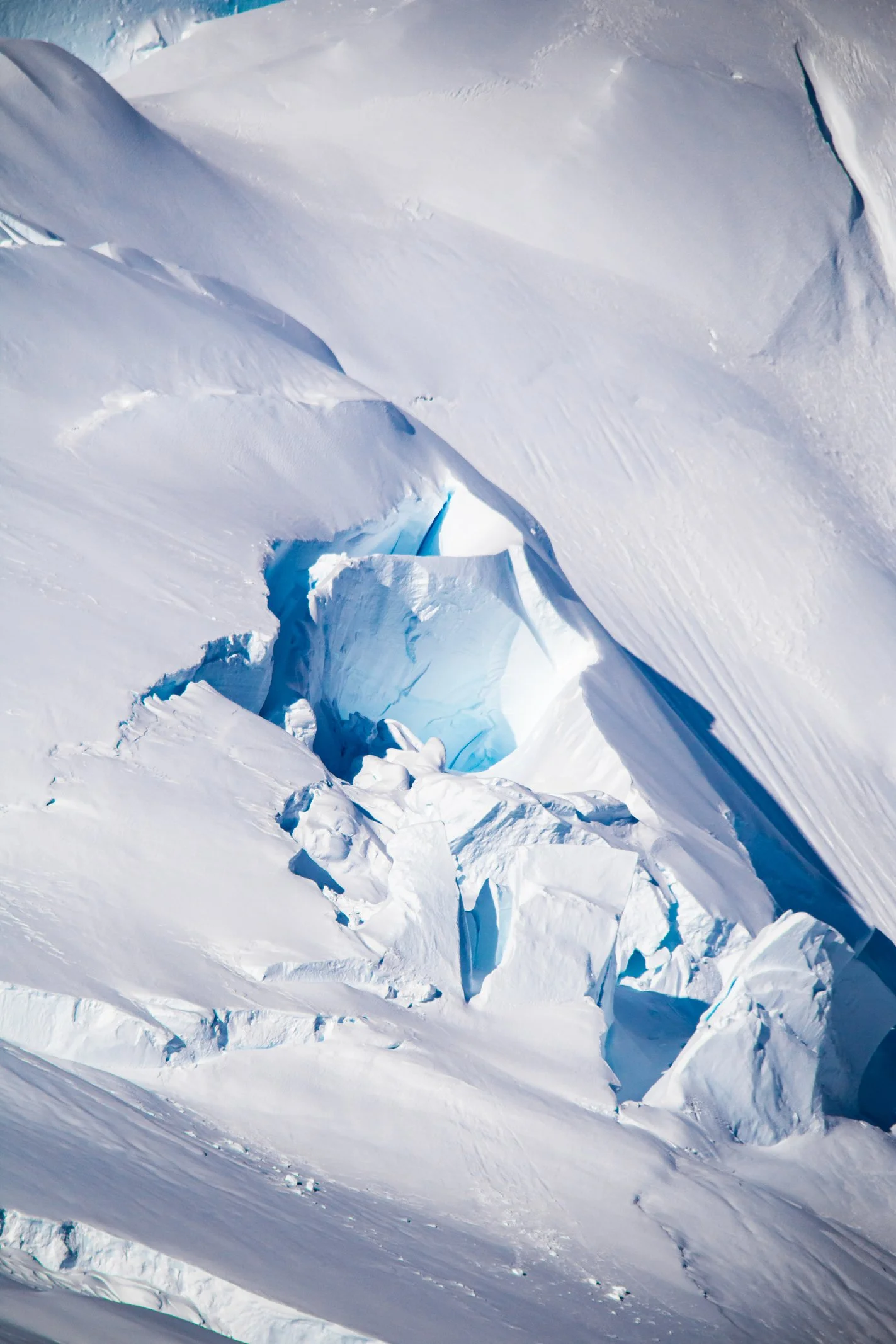 A snowy, icy landscape with large crevasses and blue ice formations in a glacial area.