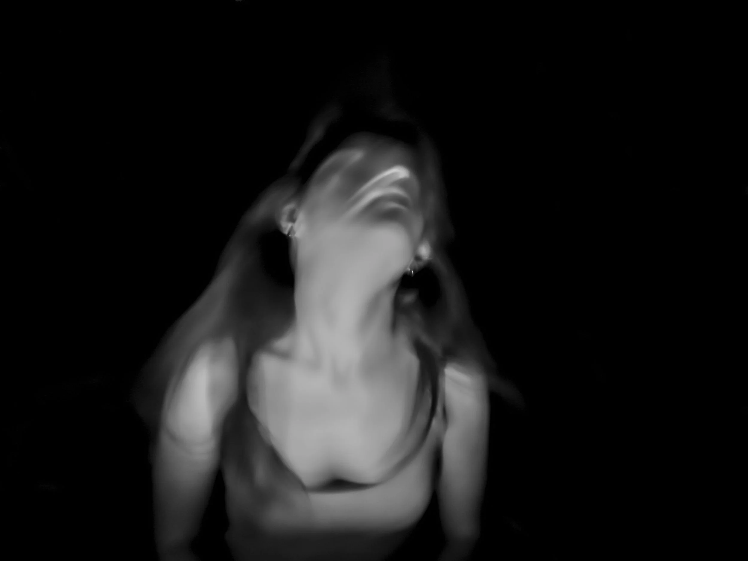 Blurred black-and-white photo of a woman with long hair, wearing earrings, with her head tilted back and eyes closed.