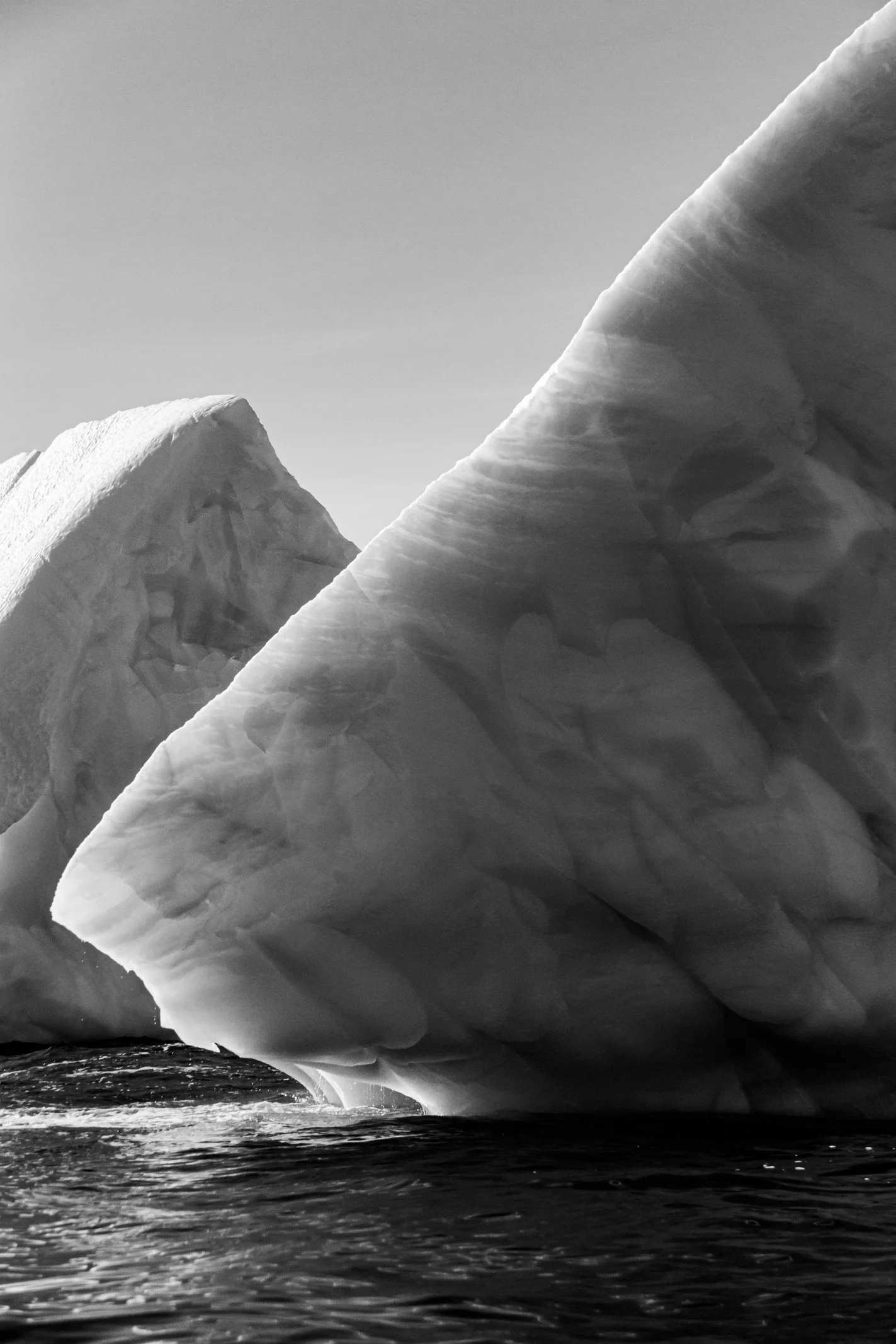 Large iceberg floating in the water with a clear sky in the background in black and white.