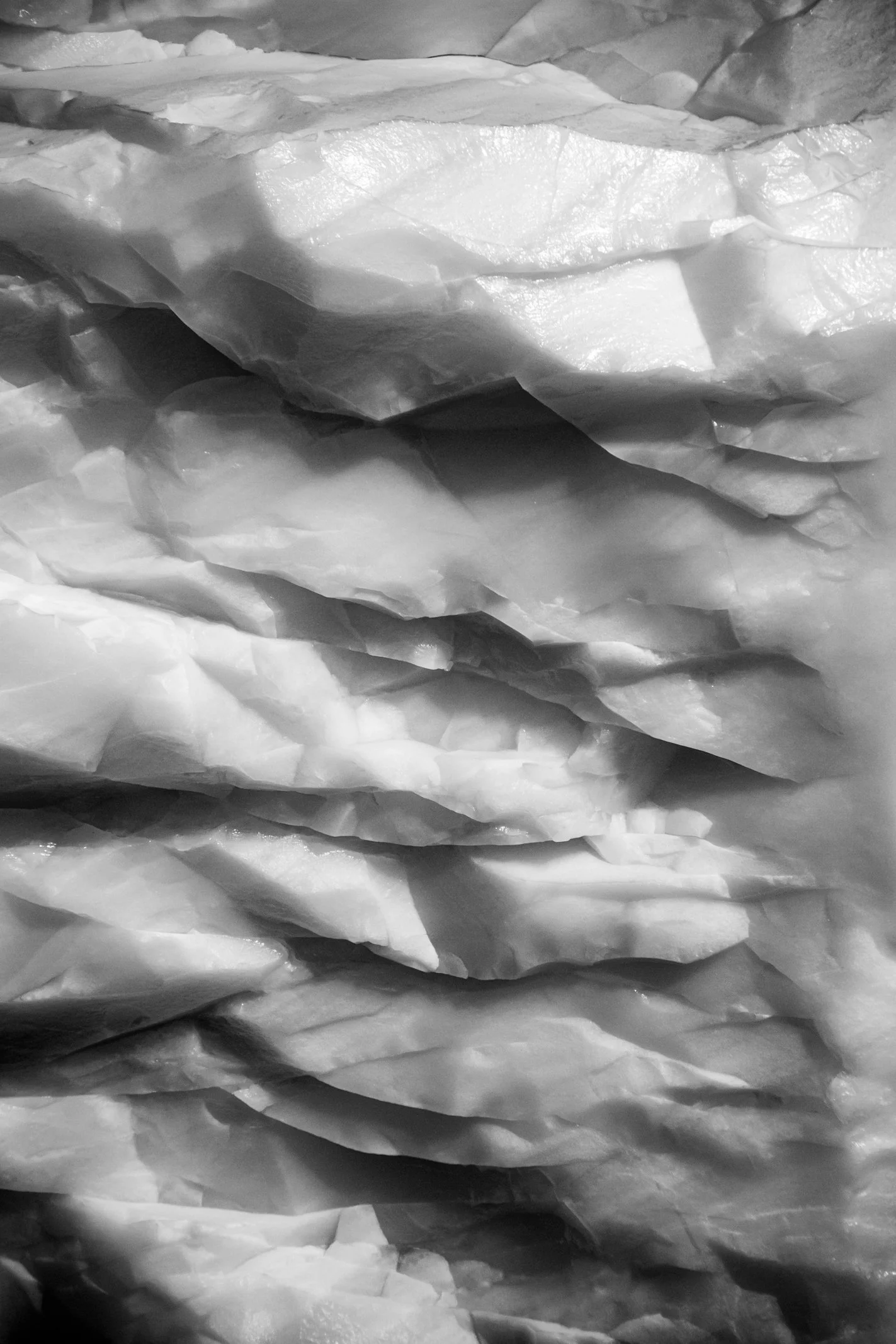 Close-up view of layered, wrinkled, icy or frozen material, possibly ice or snow, in grayscale.
