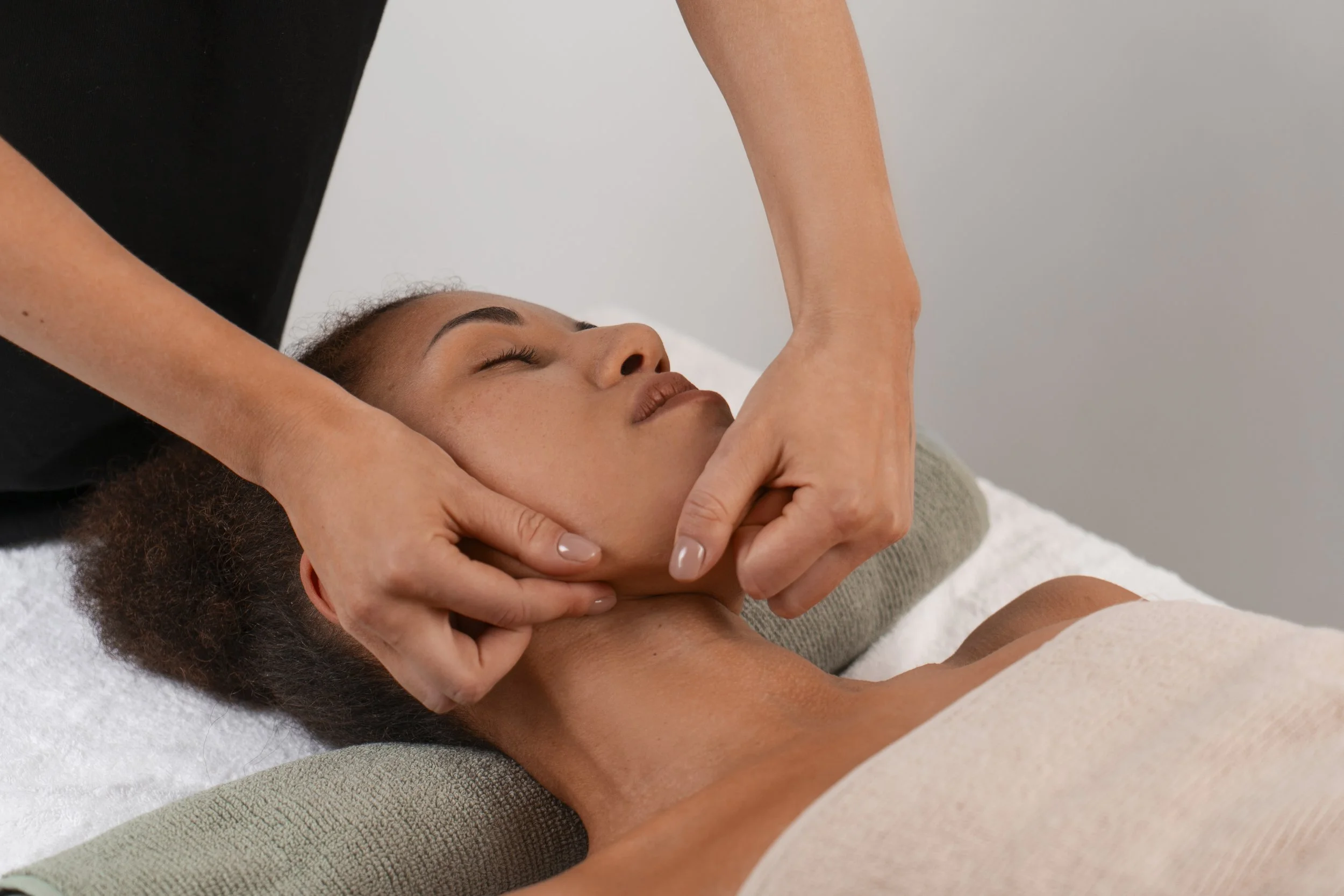 A woman receiving a facial massage from a therapist in a spa or wellness setting.