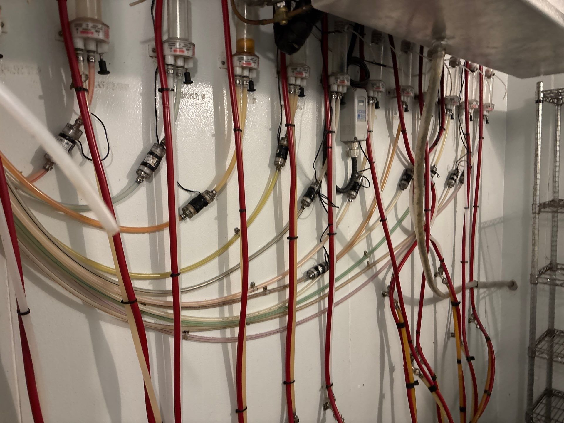 A wall with multiple transparent tubes and red, yellow, and white wires connected to various components, possibly part of an industrial or laboratory setup.