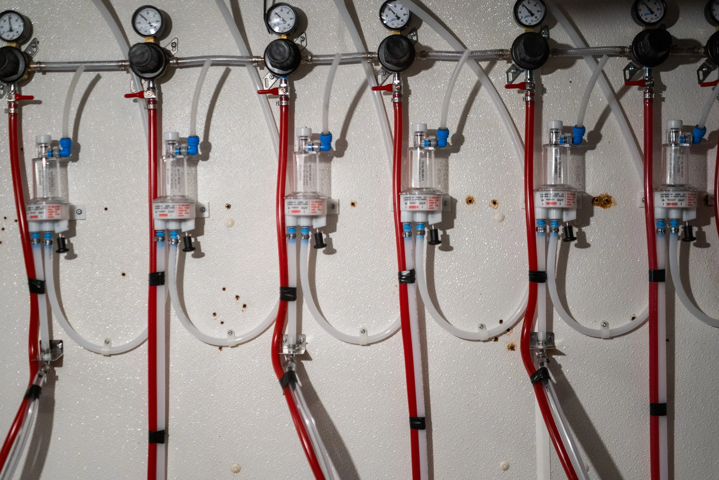 BeerSaver Metering system attached to a white wall with red and white tubing connected to them.