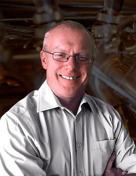 A smiling man with glasses and a white shirt, standing in front of a dark, abstract background.