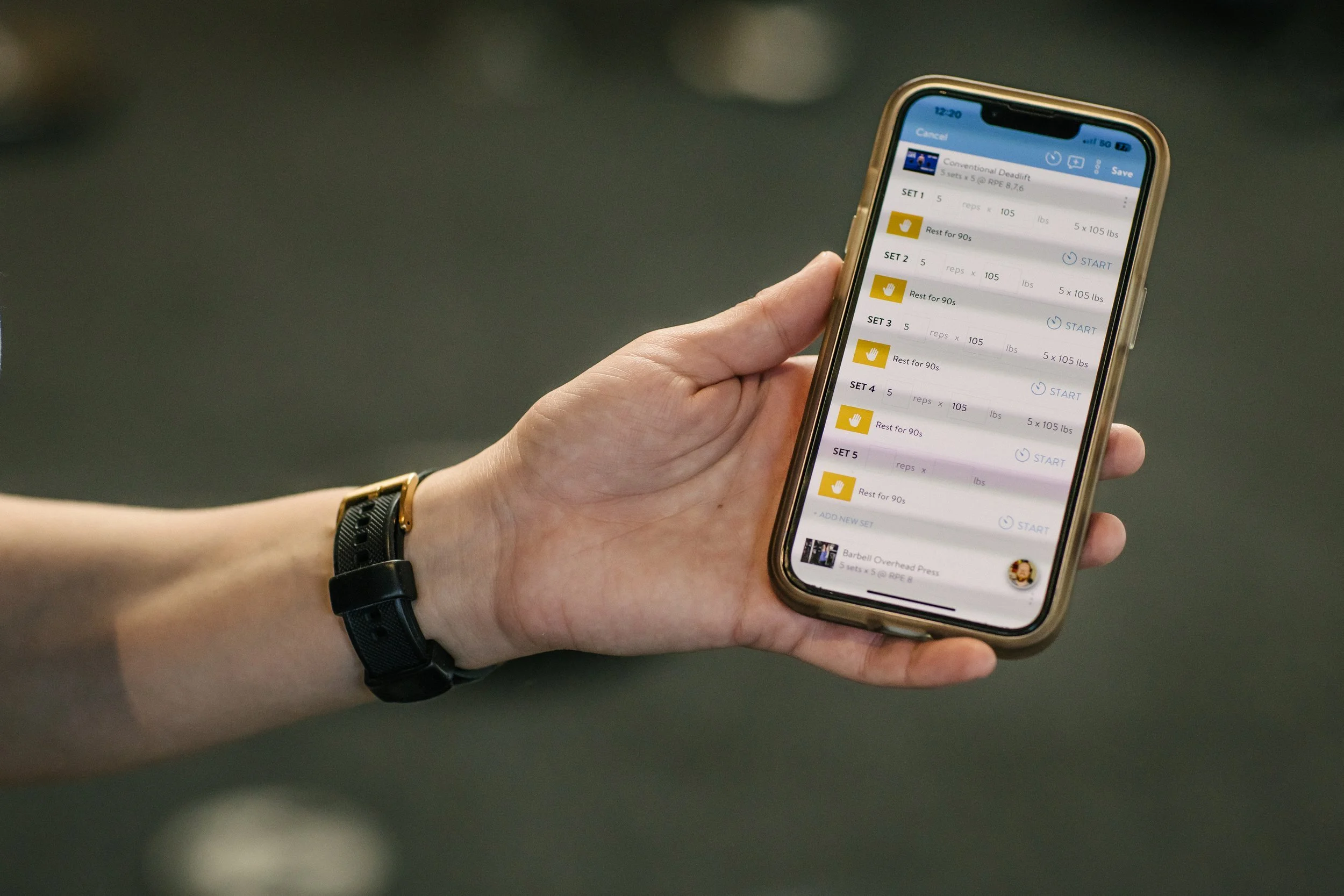 A person holding a smartphone displaying a workout app with multiple sets and rest periods.