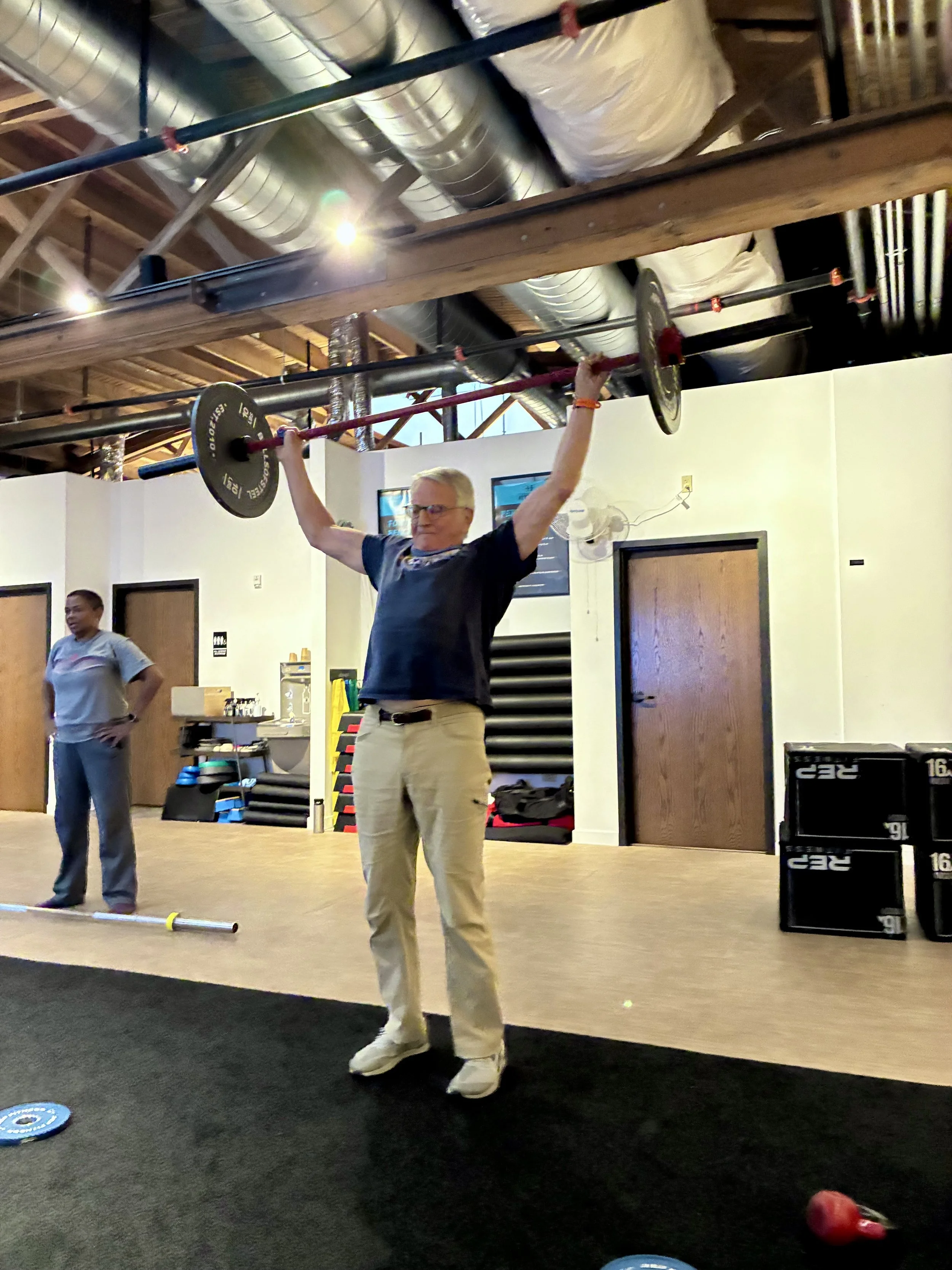 Man lifting a barbell with weights overhead during fitness training in a gym setting.