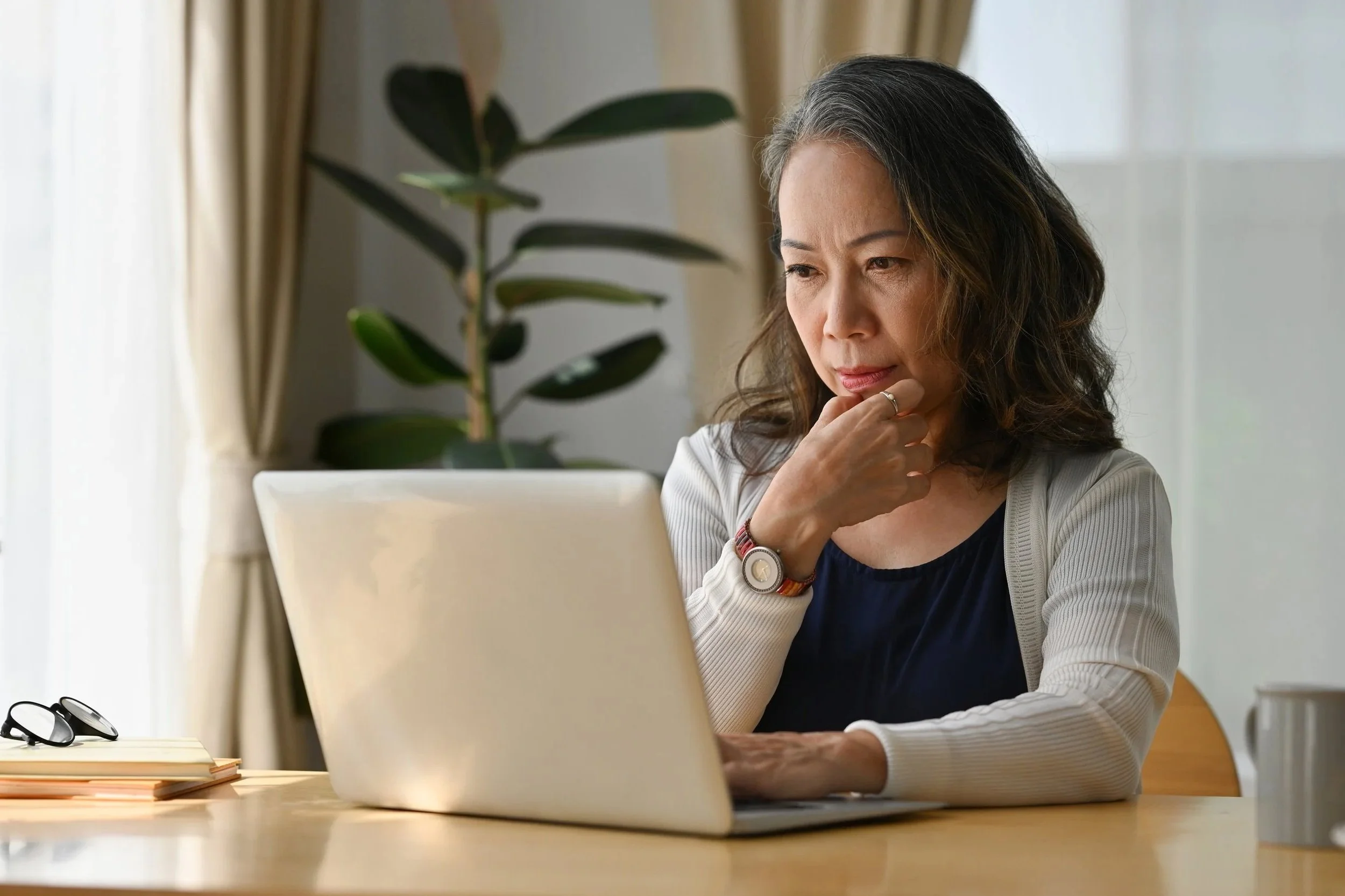 A woman sitting at a desk looking at a laptop with a pensive expression.