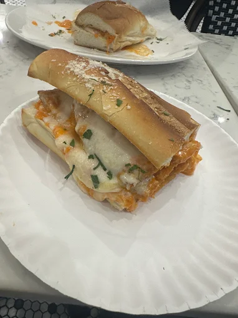 A slice of pizza with cheese, tomato sauce, and herbs on a paper plate in front of a partially eaten sandwich or calzone on a white plate.
