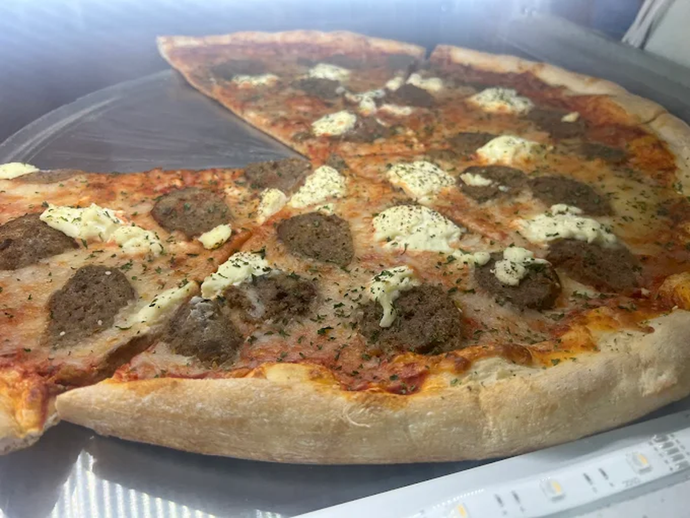 A pepperoni and sausage pizza with cheese and herbs in a plastic container.