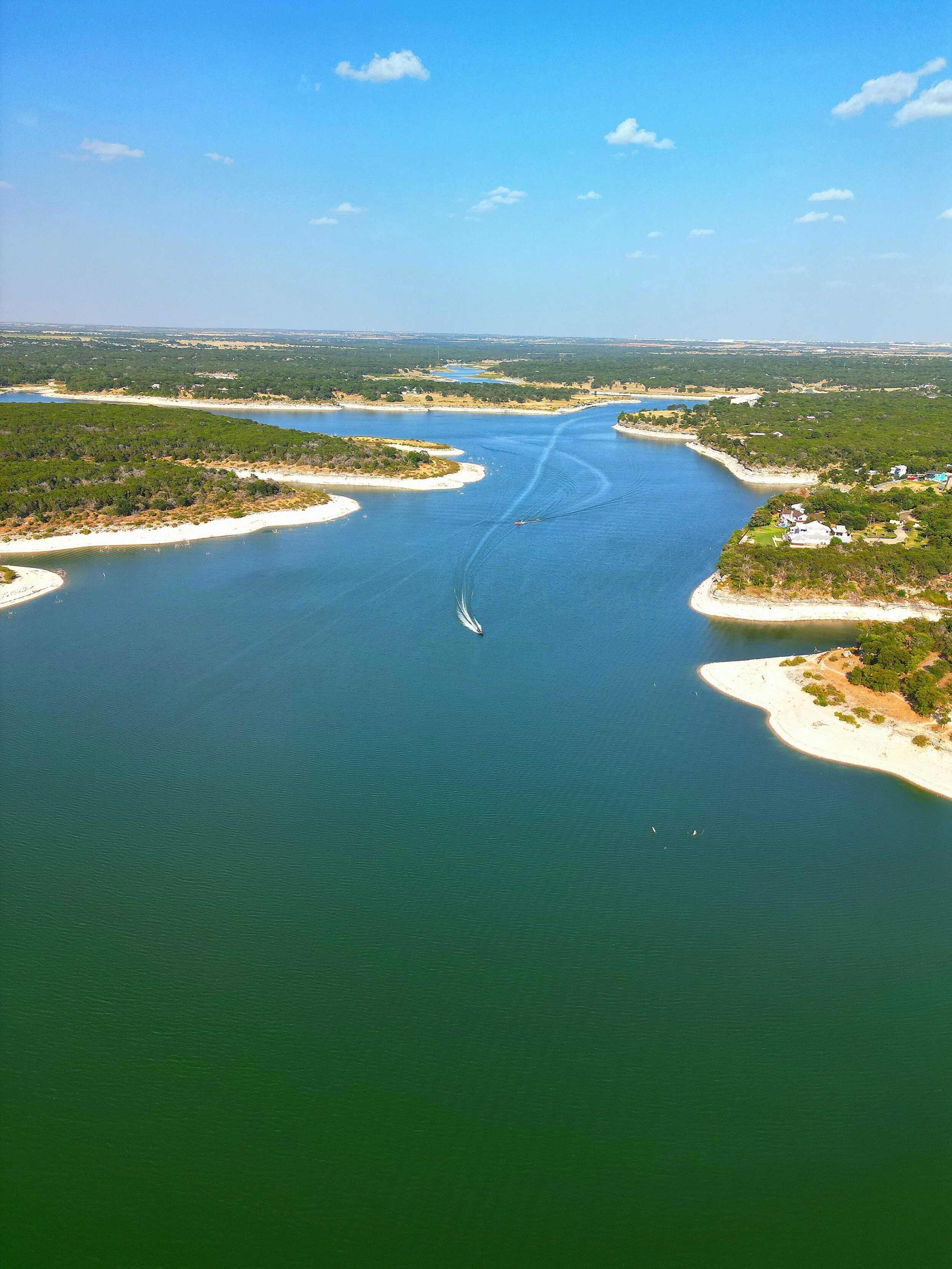 Aerial view of a river with boats sailing, surrounded by green forested areas and small landmasses.