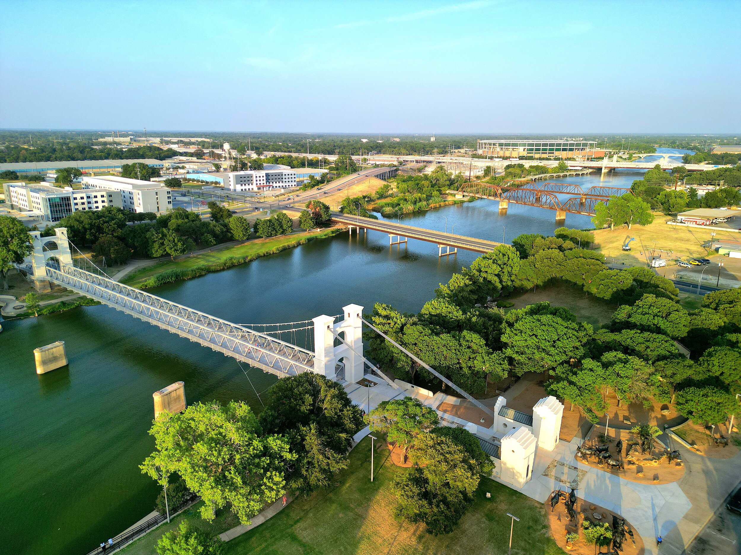 An aerial view of a city with bridges over rivers, green parks, and buildings under a clear blue sky.