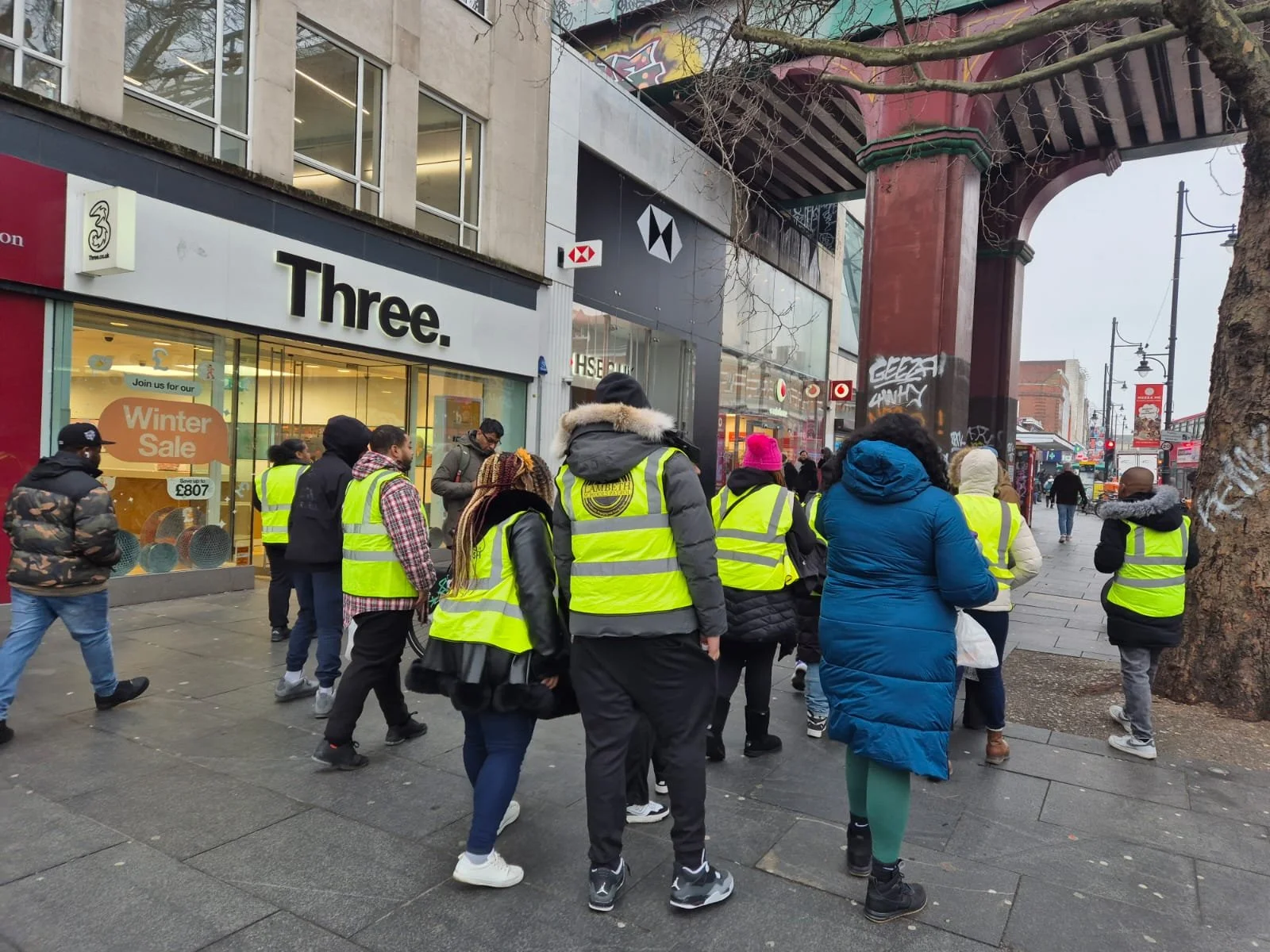 Group of people wearing yellow safety vests walking on a city sidewalk.
