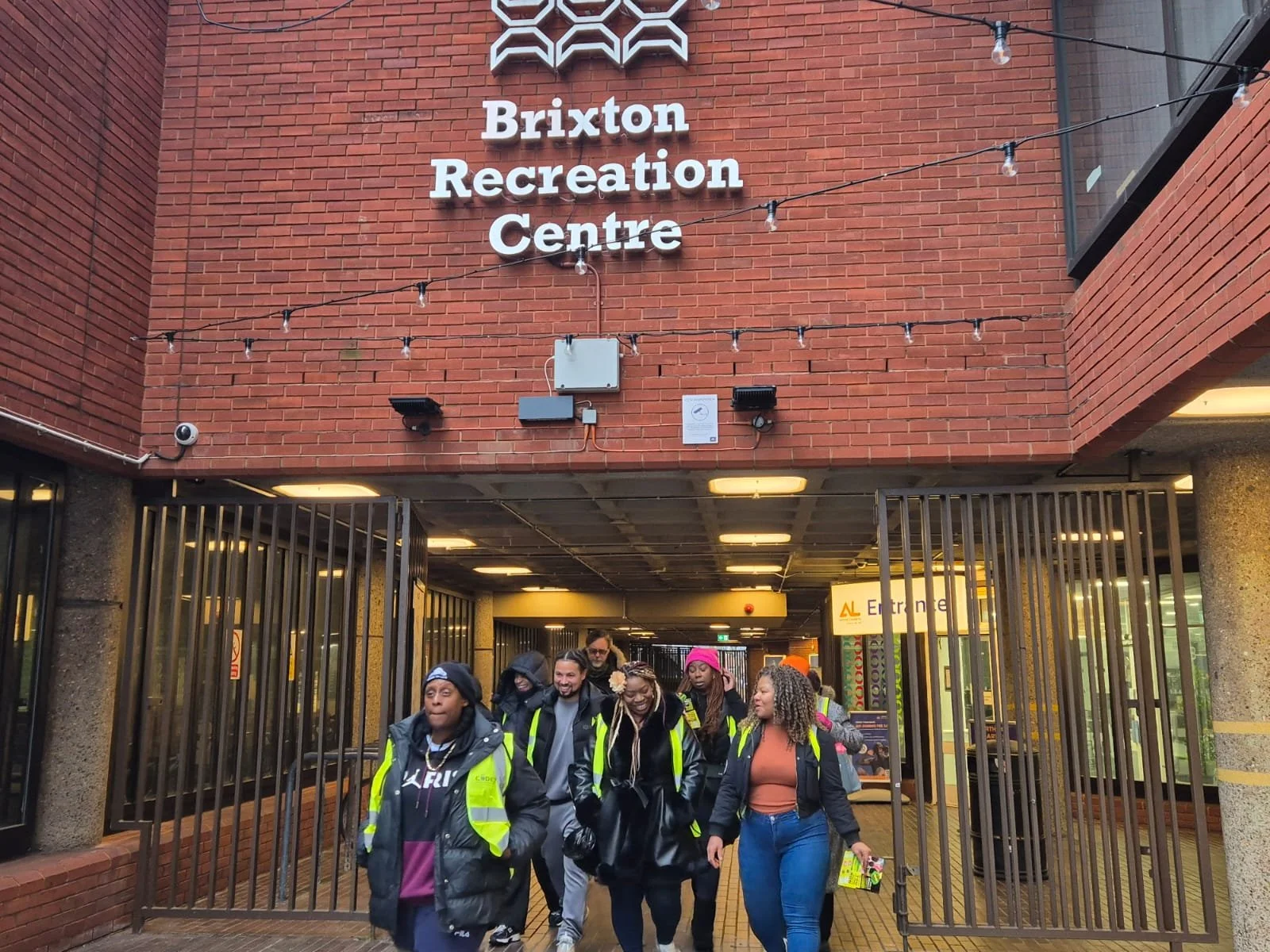 A group of people wearing high visibility vests walking out of Brixton Recreation Centre, a brick building.