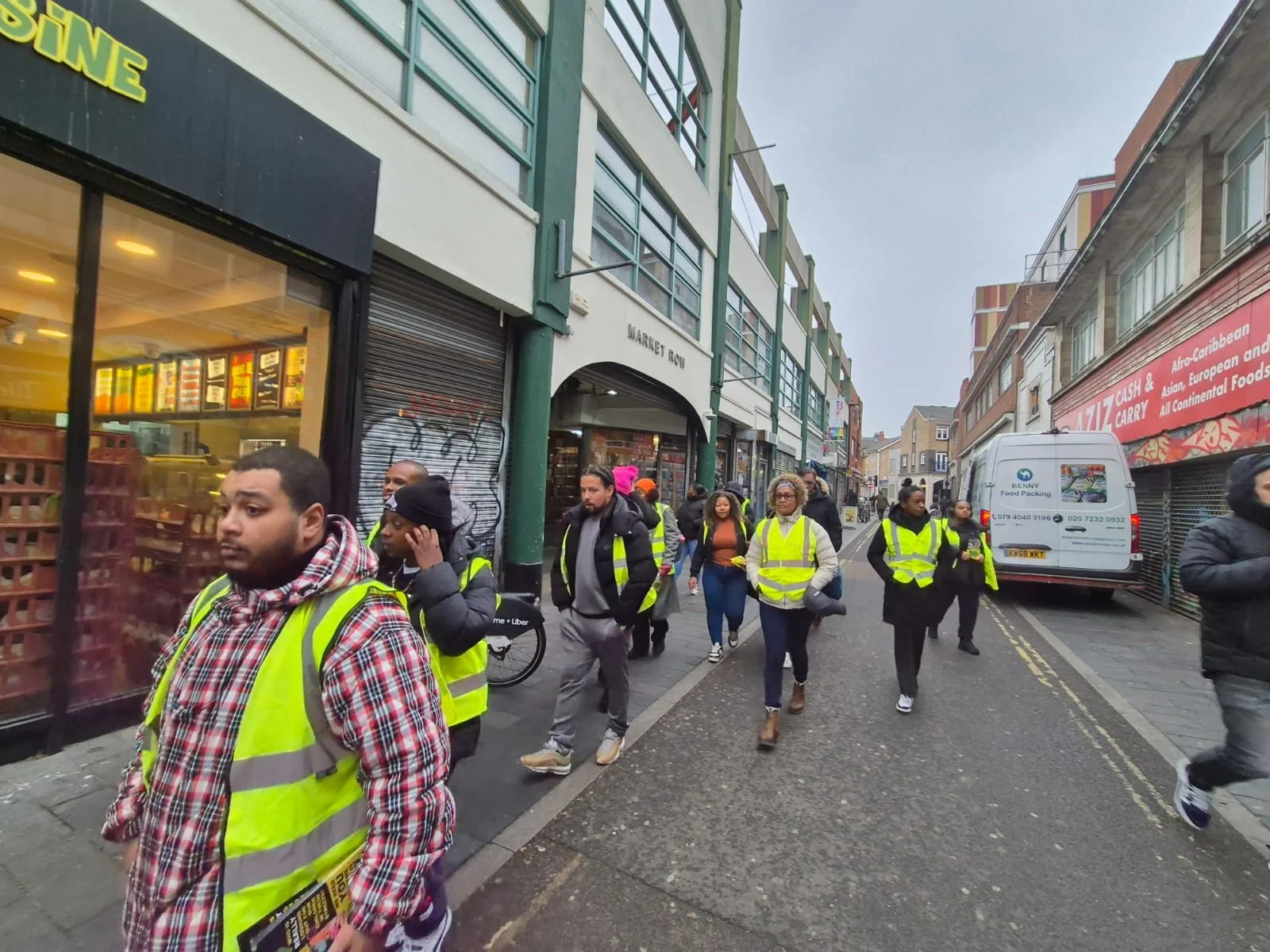 Group of people walking on a city sidewalk wearing high visibility vests.