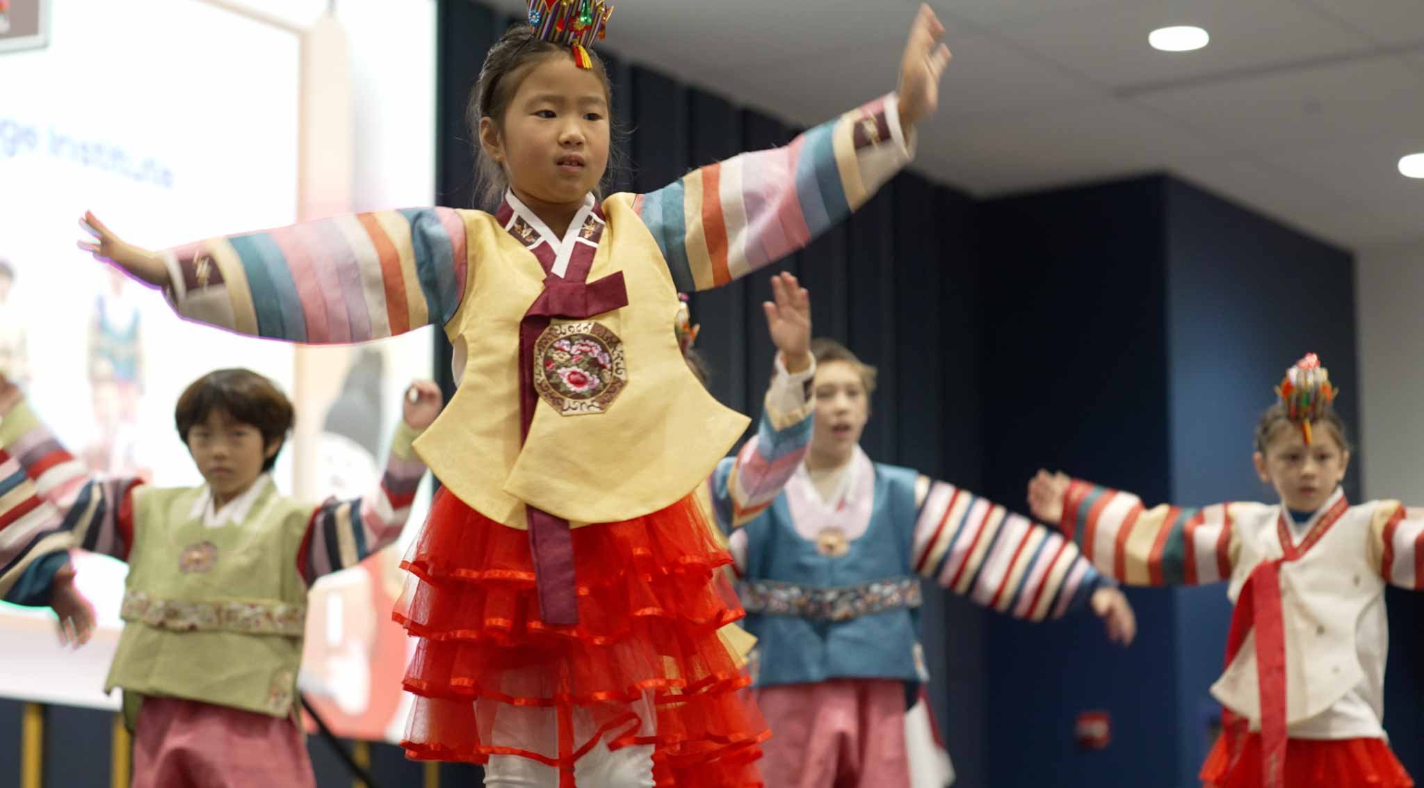 Young children performing a traditional dance in colorful Korean hanbok costumes at a cultural event.