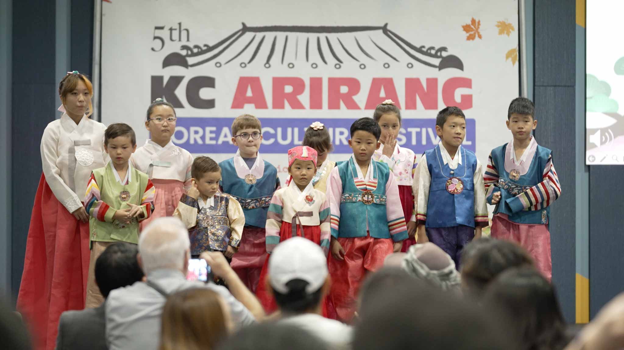 Children dressed in traditional Korean hanbok standing on stage at the 5th Korean Culture Festival, with an audience watching.