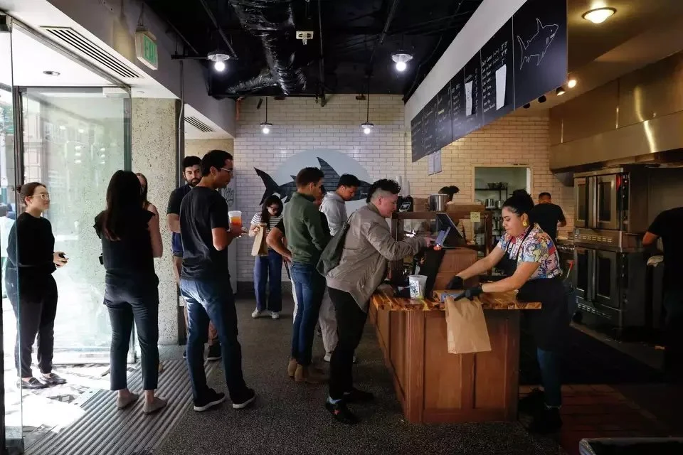 Customers line up inside a modern fast-casual restaurant with a shark mural on the back wall and a visible open kitchen.