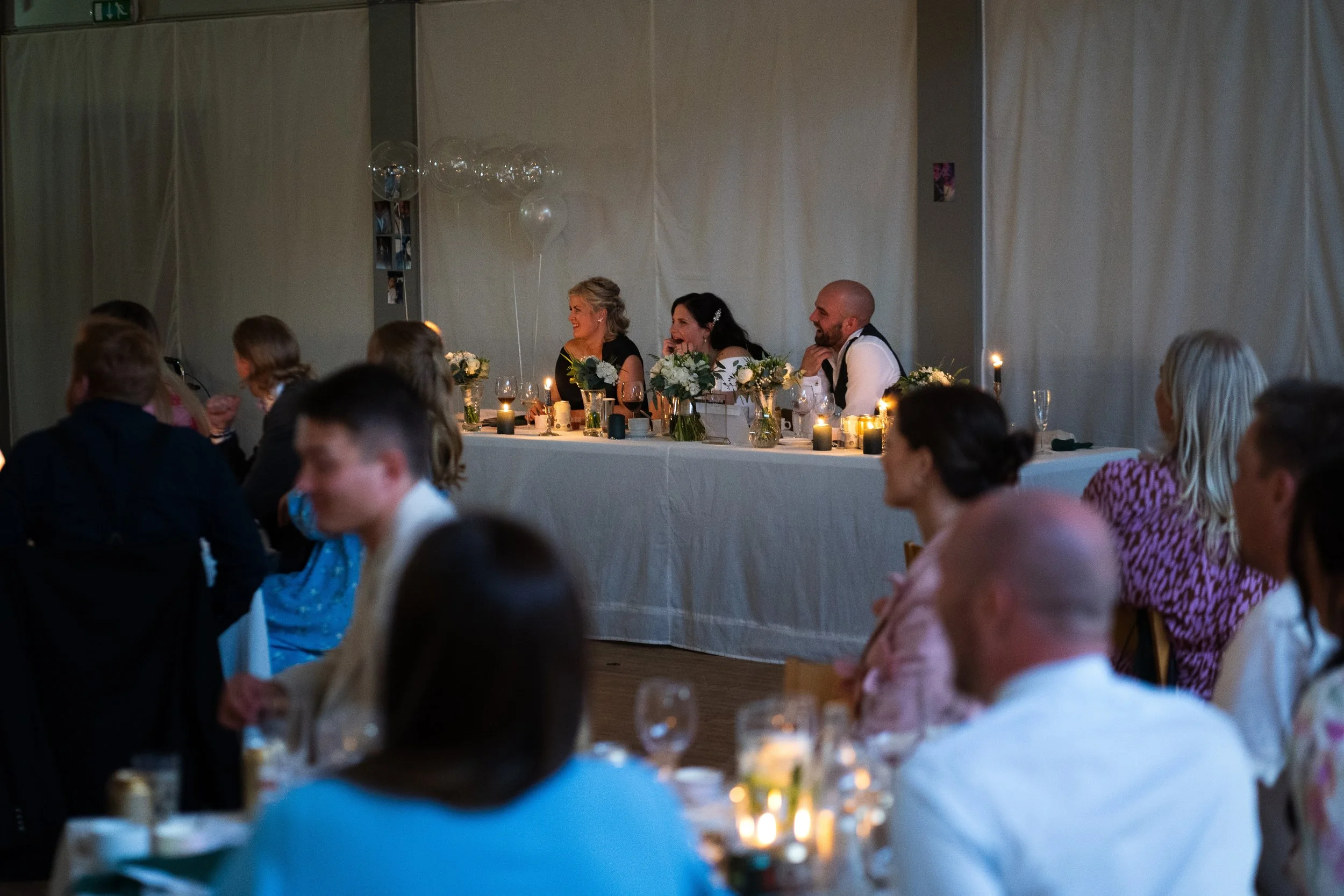Brudpar och bröllopsfest vid ett bord med blommor och ljus, under ett bröllopsevent.