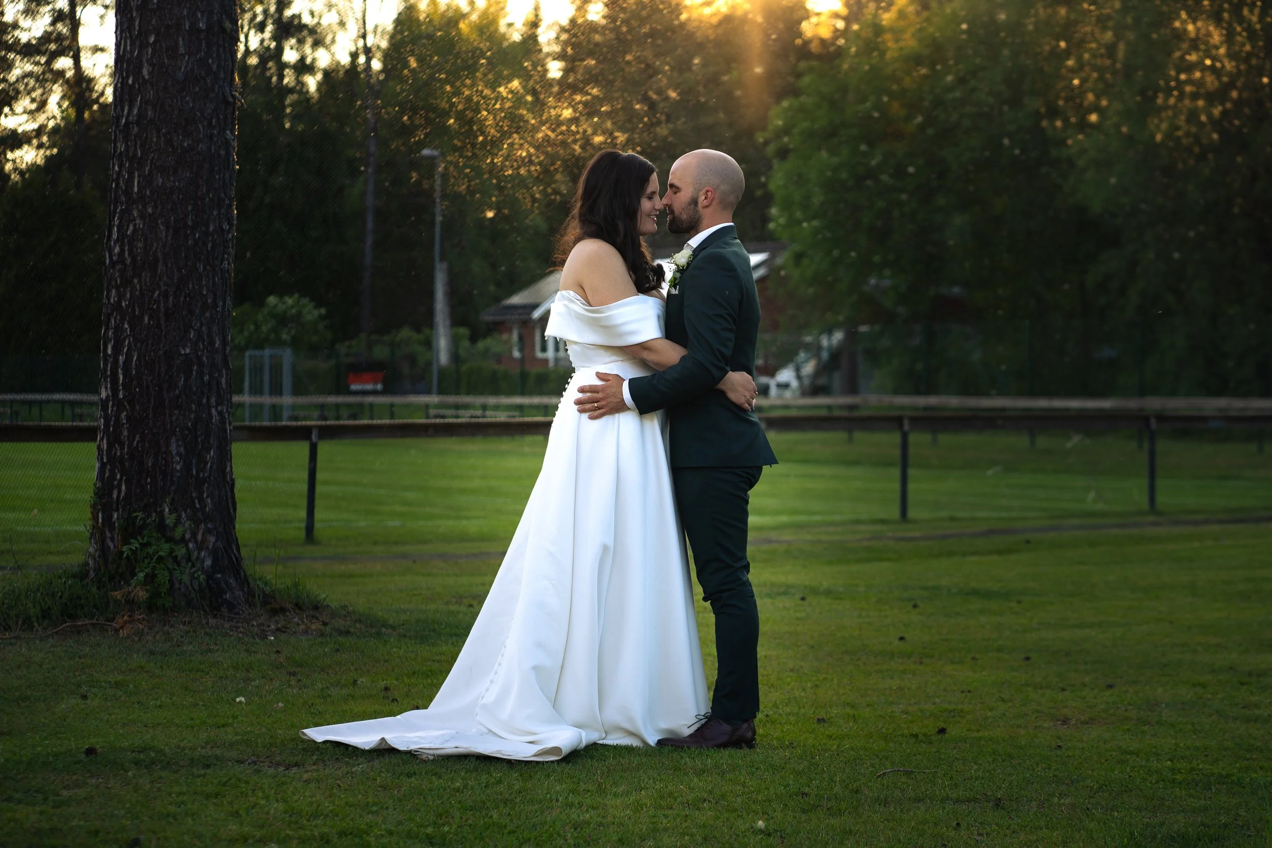 En nygift brud och groom som omfamnar varandra i en park under solnedgången.