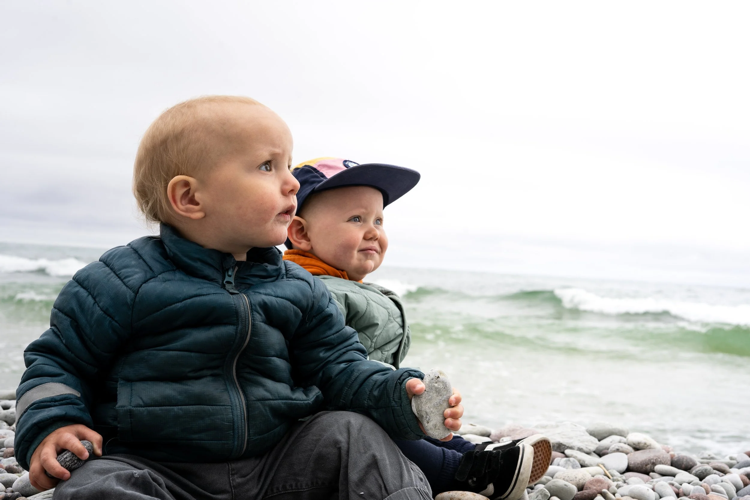 Barn som sitter på en strand och håller i en sten.