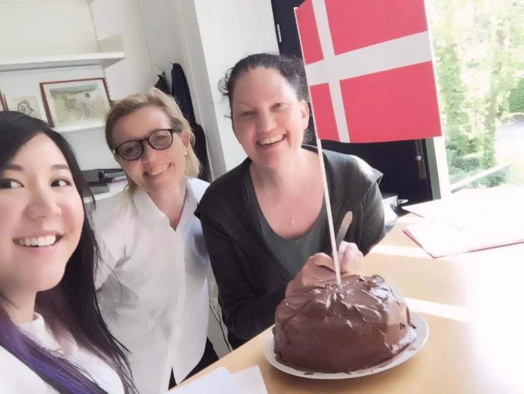 Kate MacCrimmon smiling with Denmark colleagues celebrating with chocolate cake.