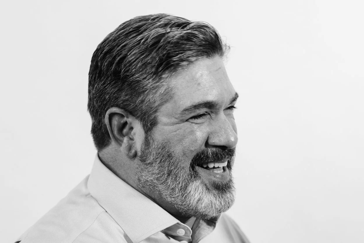 Black and white photo of a middle-aged man with gray hair and beard, smiling.