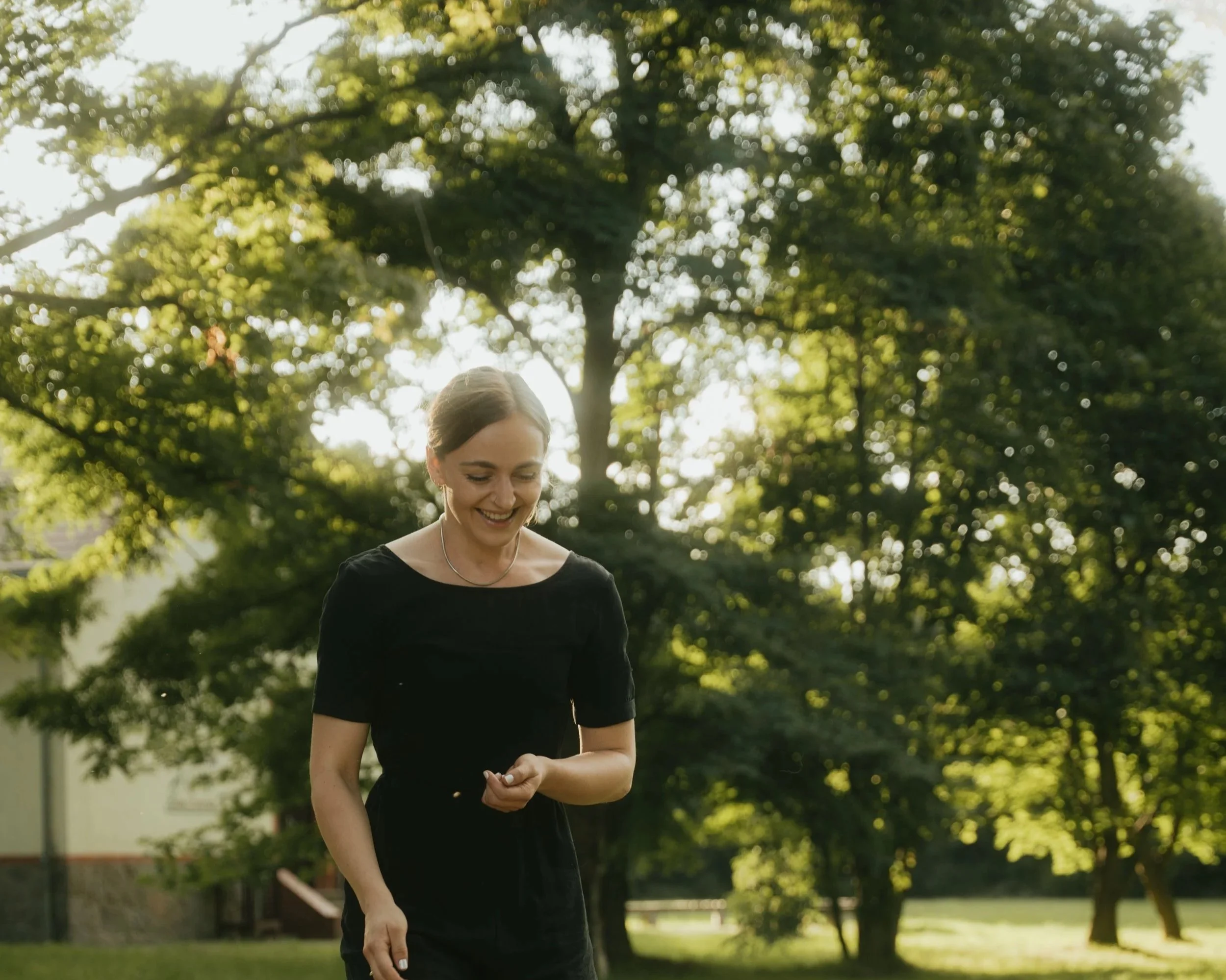 Antonia Grüner, Ordnungscoach, in schwarzer Kleidung, die im Freien bei Sonnenschein vor einem Baum steht.