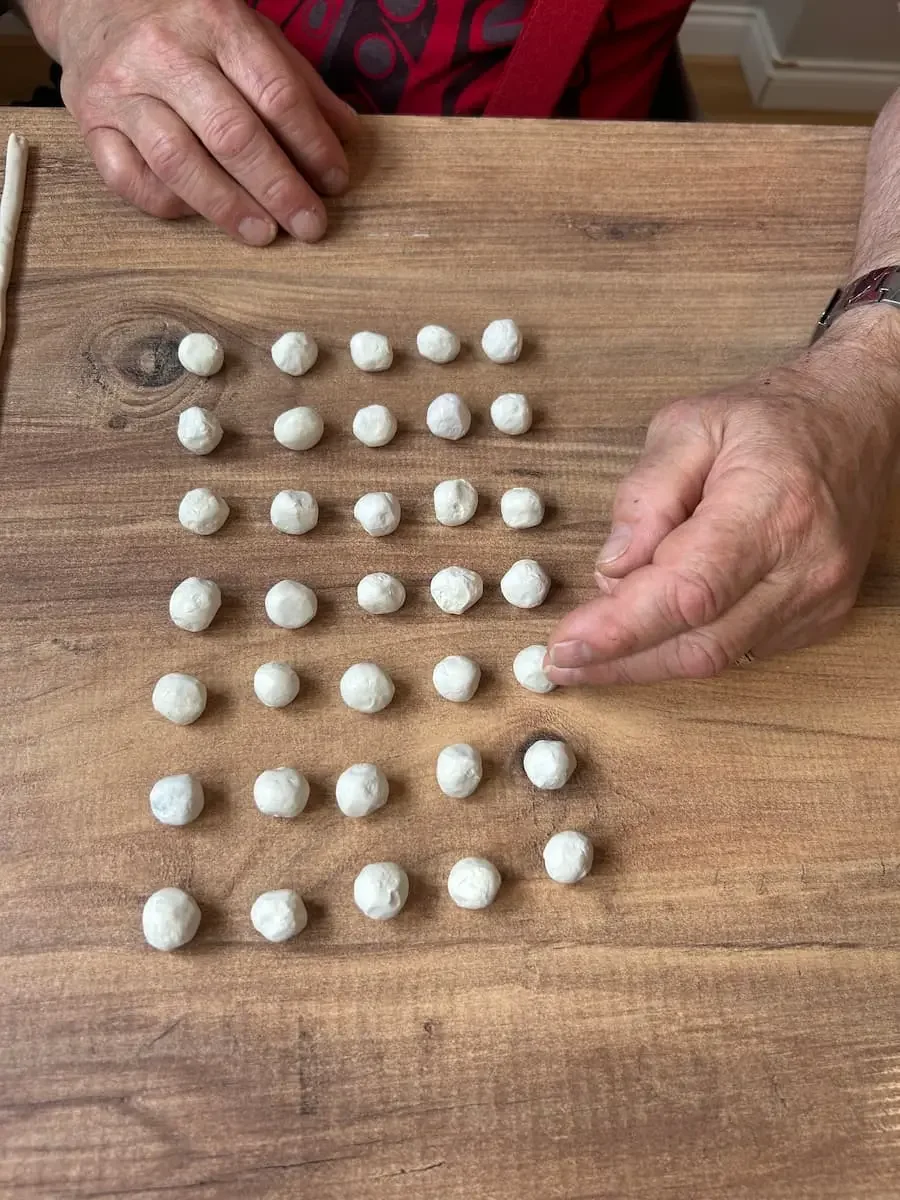 A person arranging clay balls into rows of 5 x 7 on a wooden table.
