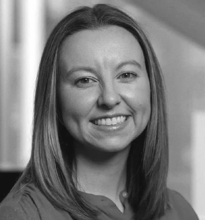 Black and white photo of a smiling woman with shoulder-length straight hair, wearing a collared shirt.