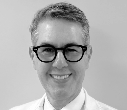 Black and white photo of a man with glasses, and a broad smile, wearing a white shirt.