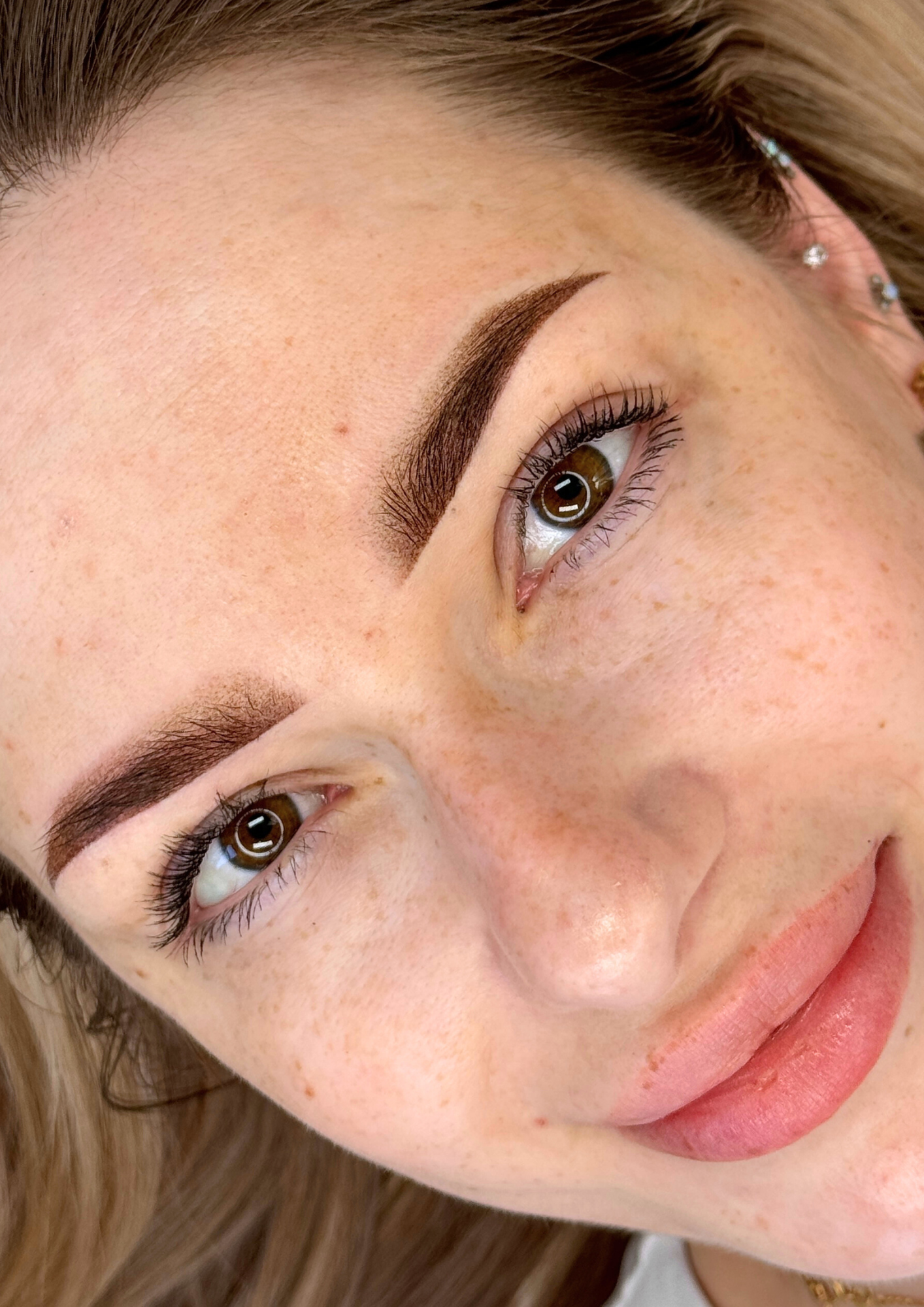 Close-up of a woman's face showing her brown eyes, well-groomed eyebrows, fair skin with freckles, and subtle makeup.