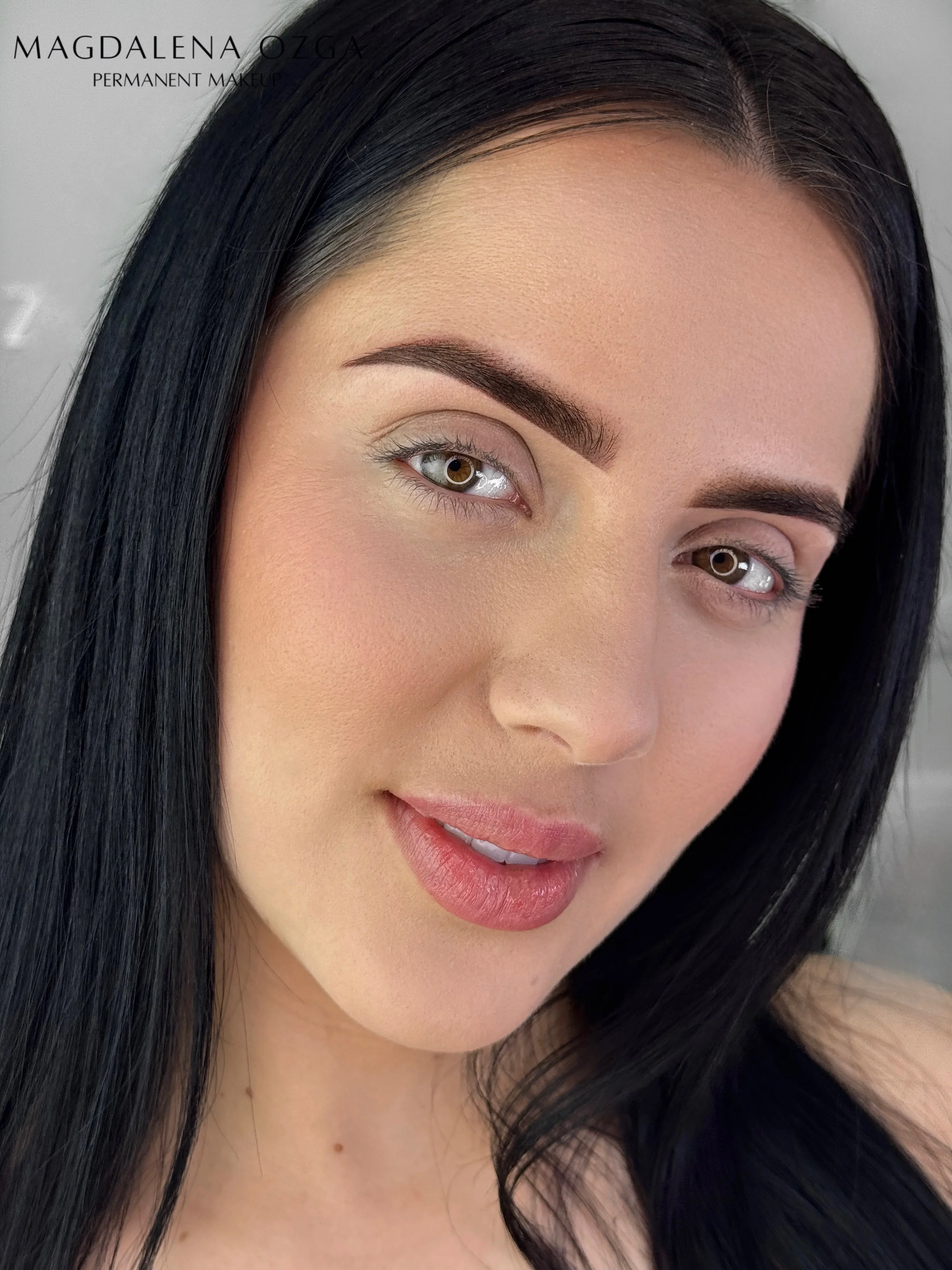 Close-up portrait of a woman with long black hair, brown eyes, and light makeup, smiling gently.