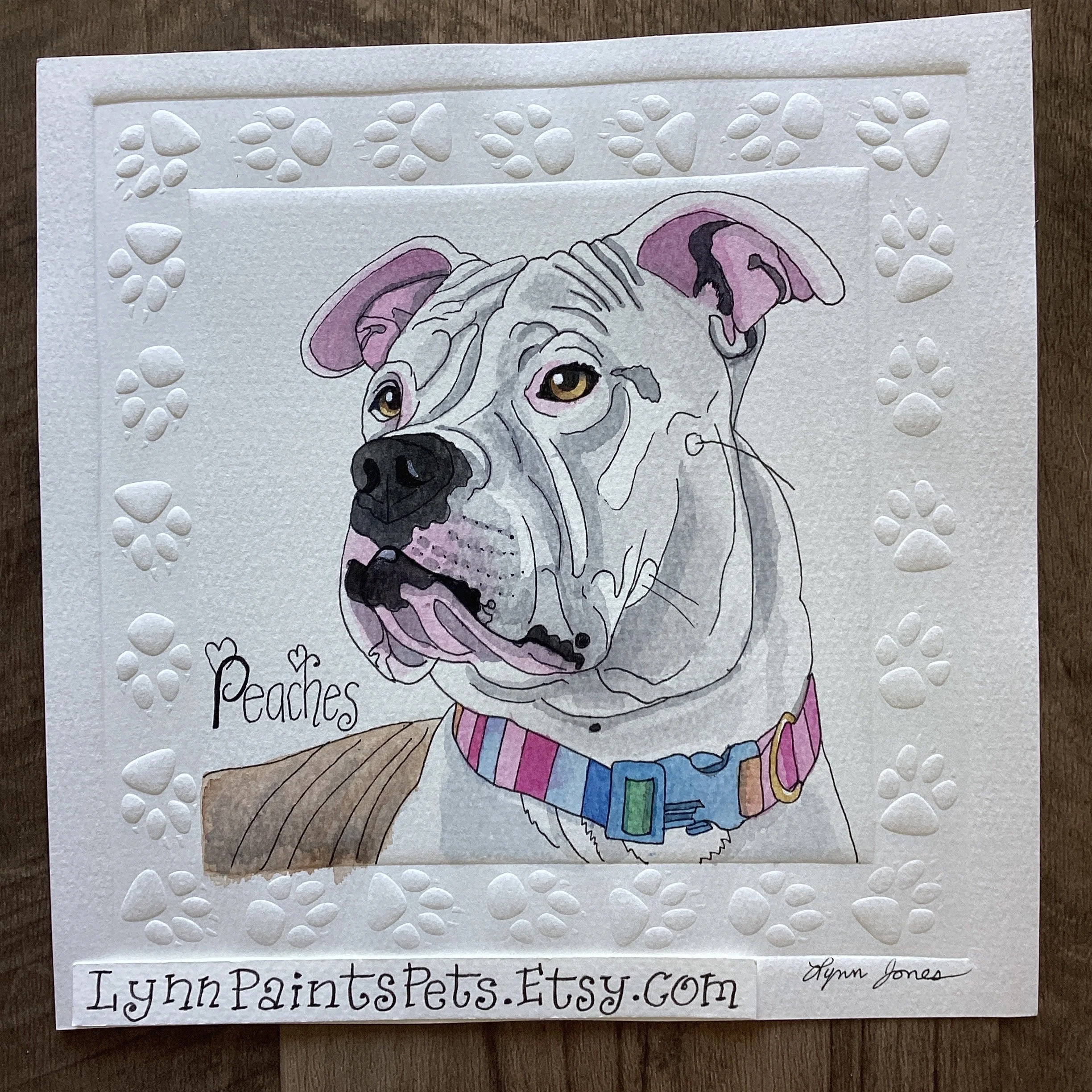 A painting of a gray pit bull named Peaches, wearing a colorful collar, with a pink tongue showing, created by Lynn Jones, with a white border decorated with embossed paw prints, and the website LynnPaintsPets.Etsy.com written at the bottom.