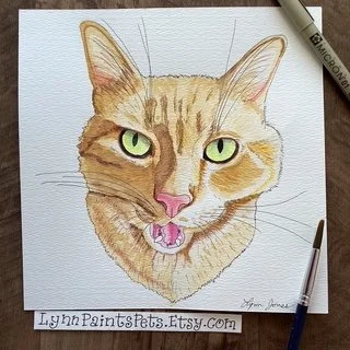 Watercolor painting of a cat with green eyes, pink nose, and open mouth showing teeth, on textured paper.