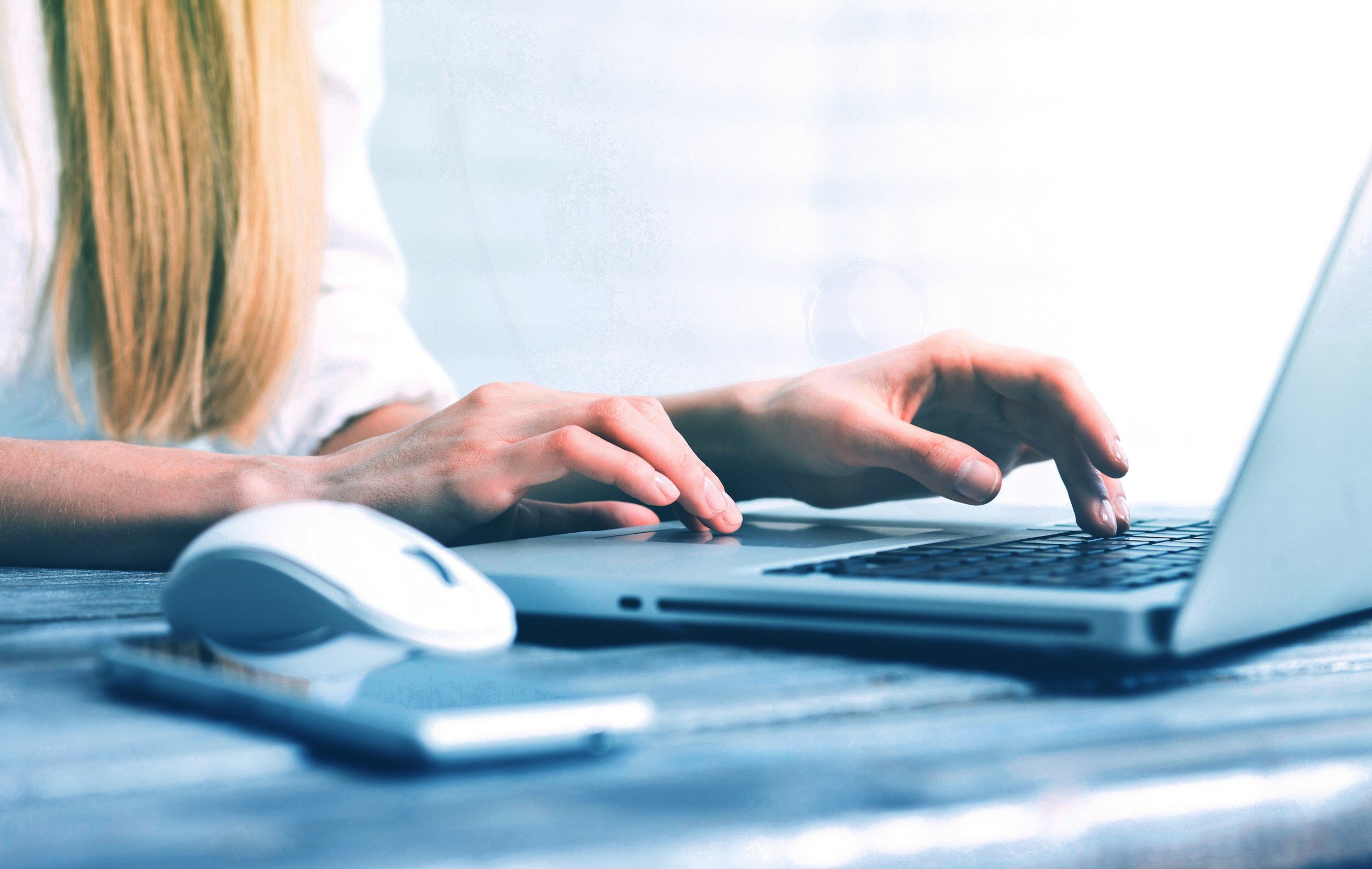 Desk with computer, mouse, and phone with a woman's hands typing on the keyboard