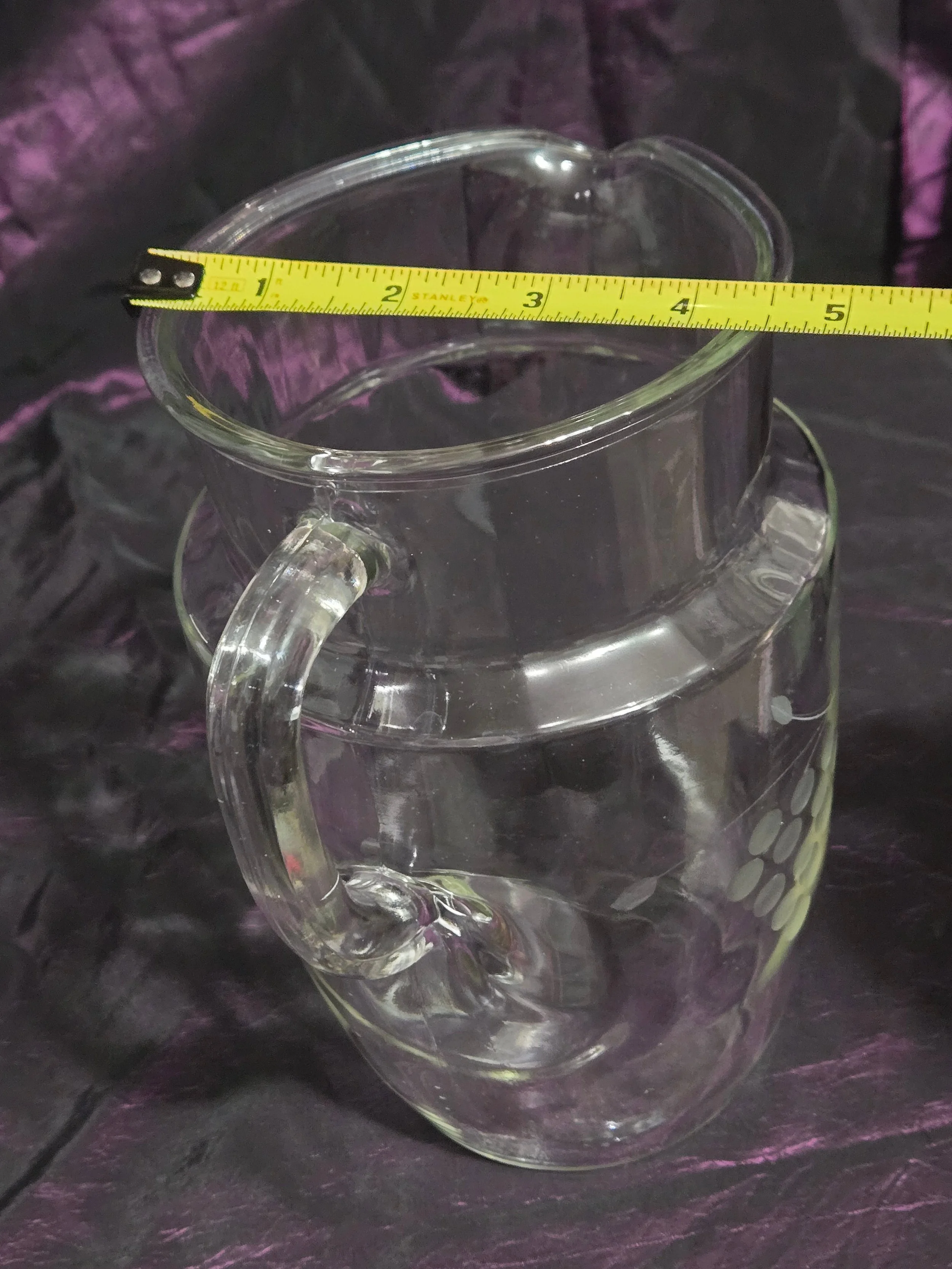 Clear glass pitcher etched with grapevine and crown designs, vintage mid-century style with curved handle and flared spout.