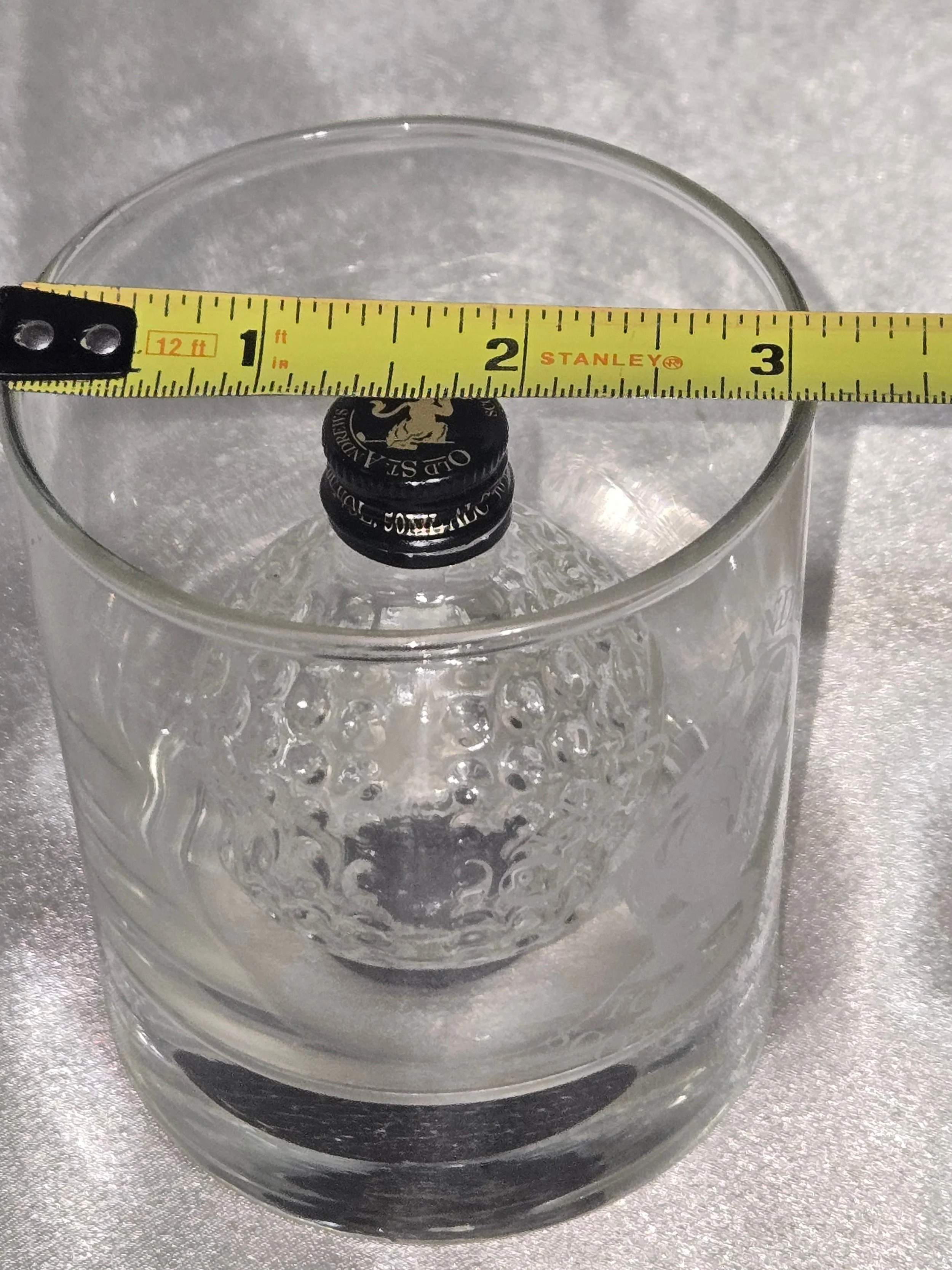 Side angle showing embossed golf ball texture of bottle inside rocks glass out of packaging showing measurements