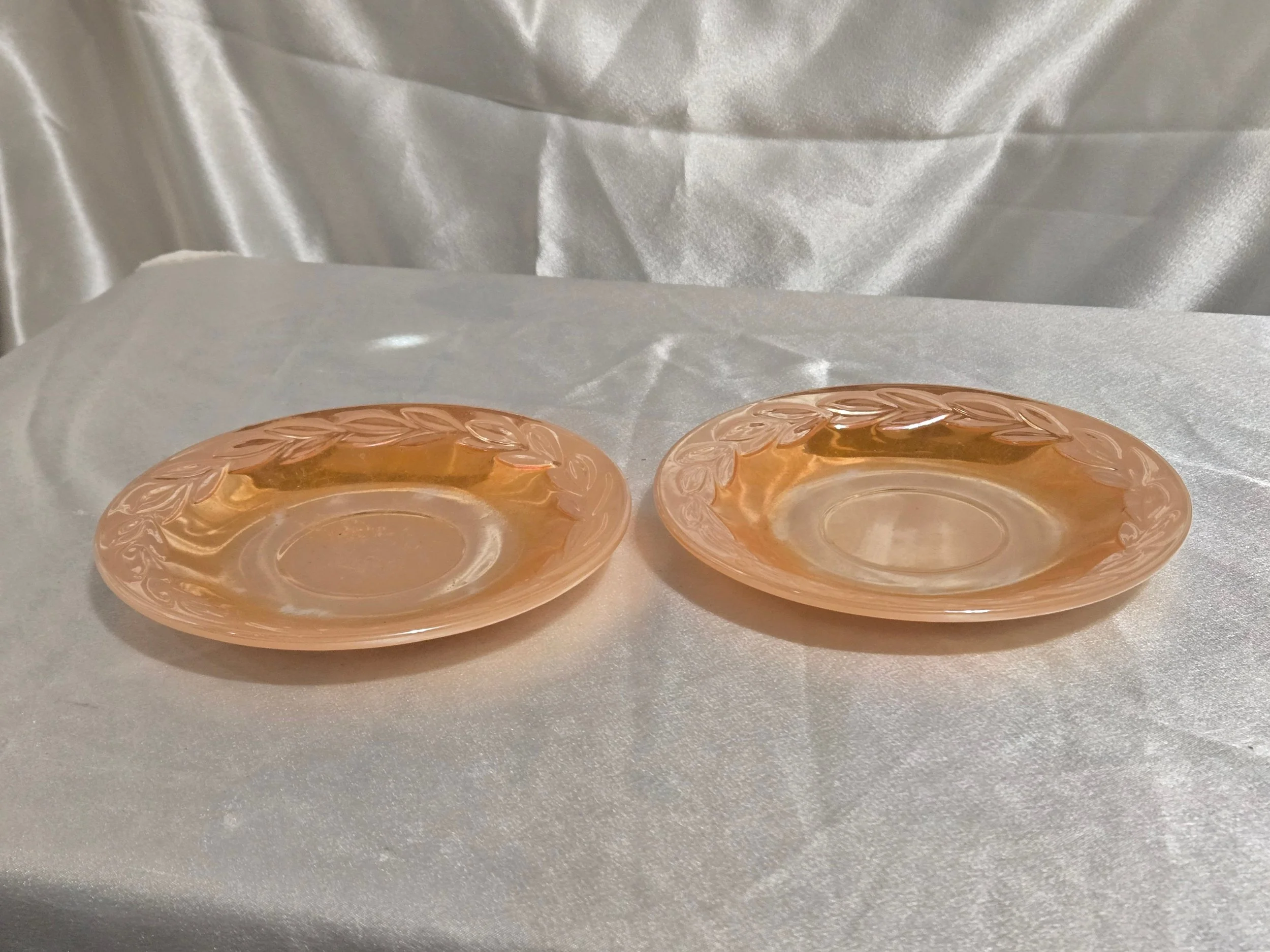 Set of Fire-King Peach Lustre saucers with iridescent sheen and vintage mid-century glow against white background.