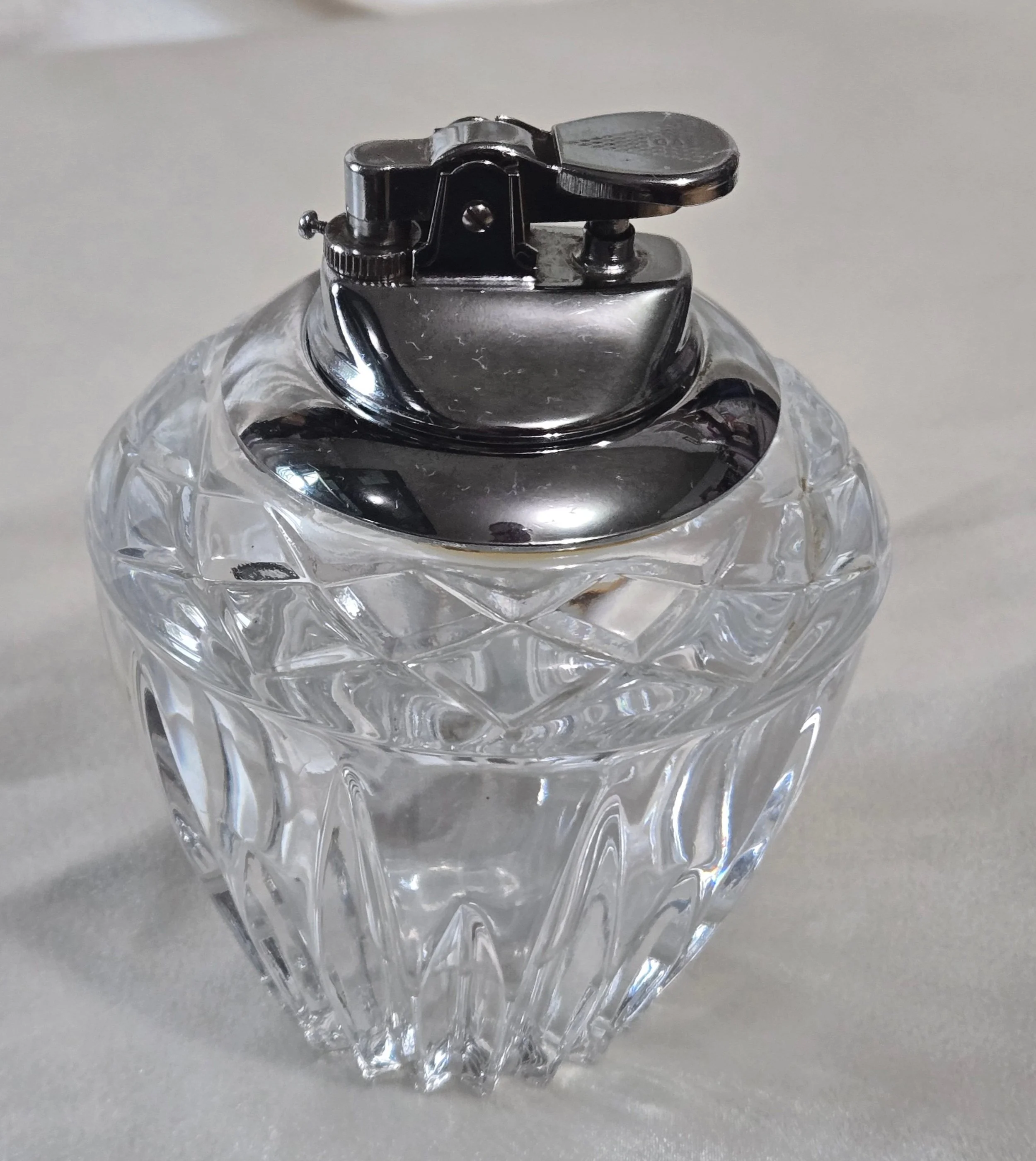 Close-up of a crystal tabletop lighter with a decorative pattern and chrome finish.