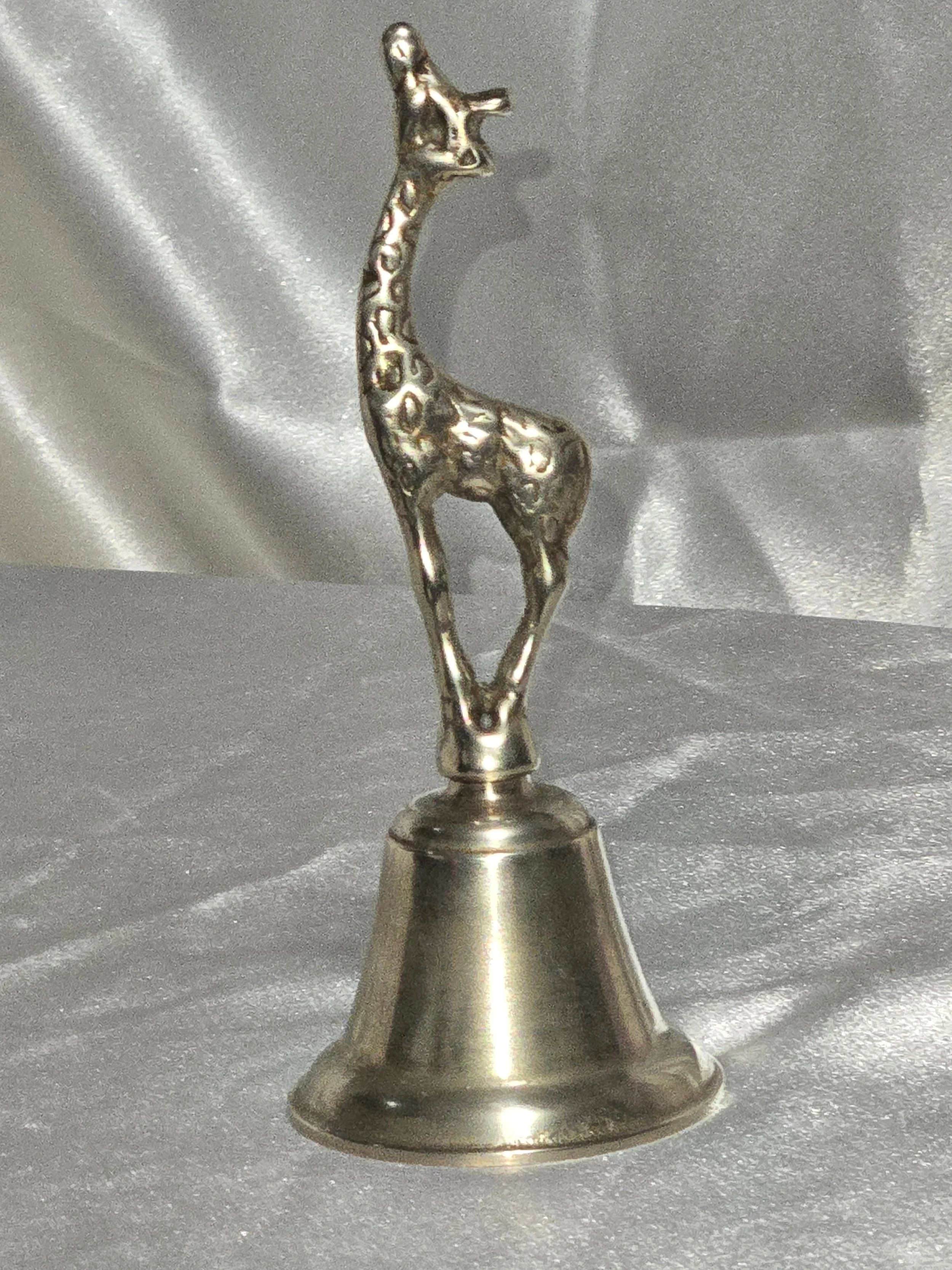 Close-up of vintage brass giraffe-shaped bell standing on silver background, 6 in tall mid-century safari collectible. Left facing full side view