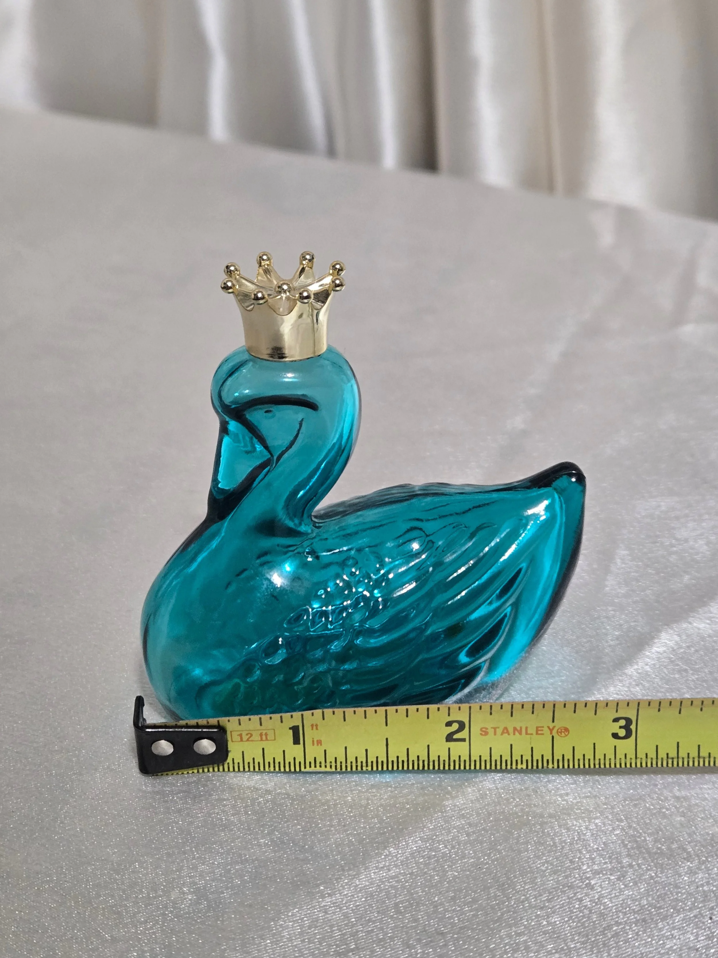 Side profile of teal glass Avon swan perfume bottle showing elegant curved neck and wing detail.