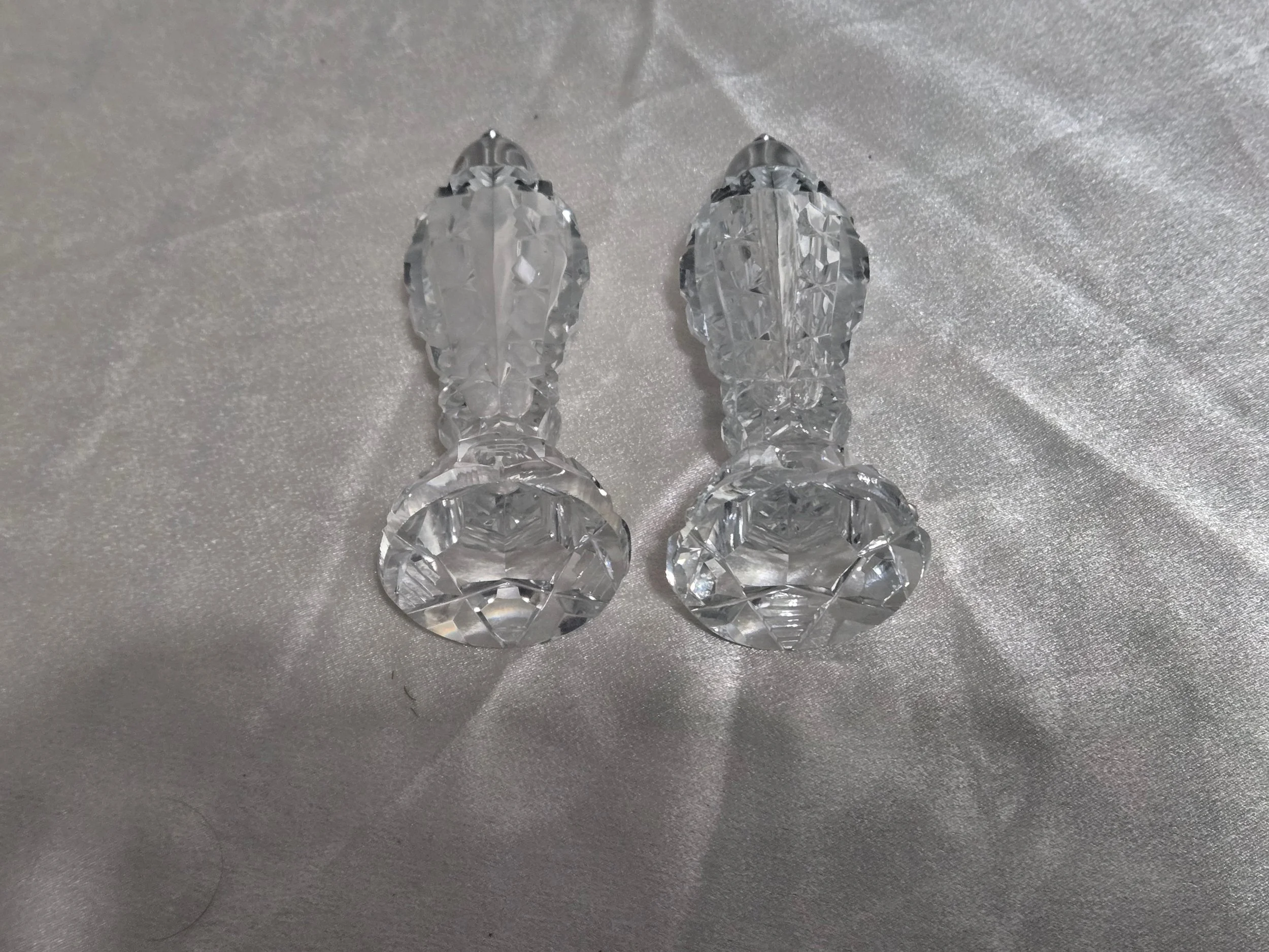 Matching crystal salt and pepper shakers displayed side by side on satin background