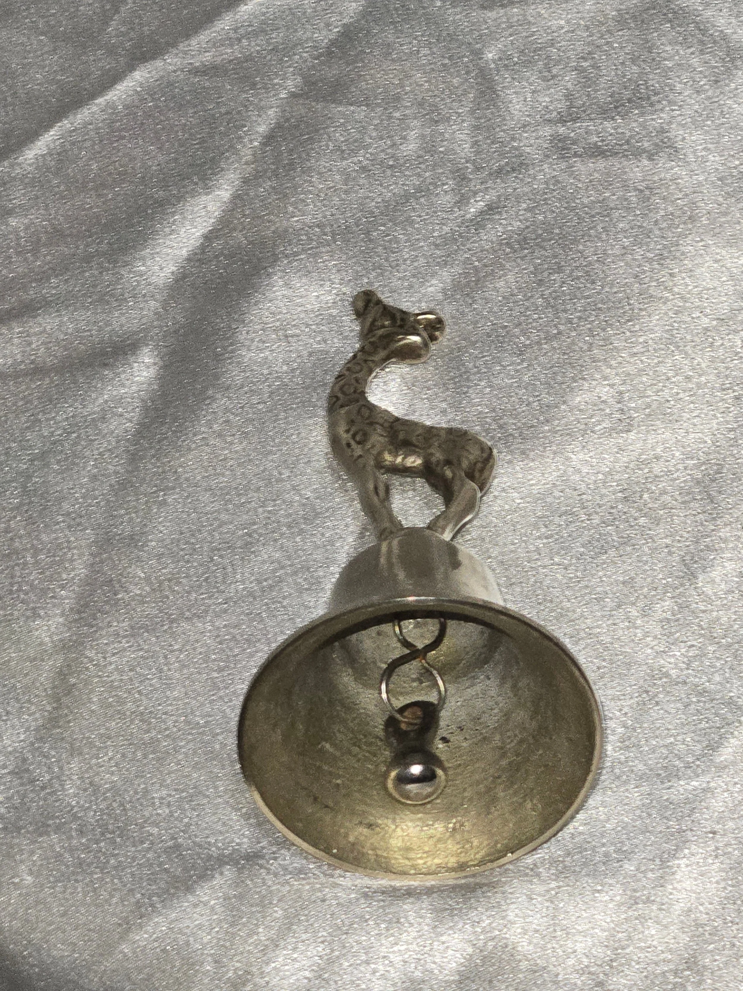 Close-up of vintage brass giraffe-shaped bell standing on silver background, 6 in tall mid-century safari collectible. Laying full front and bottom view