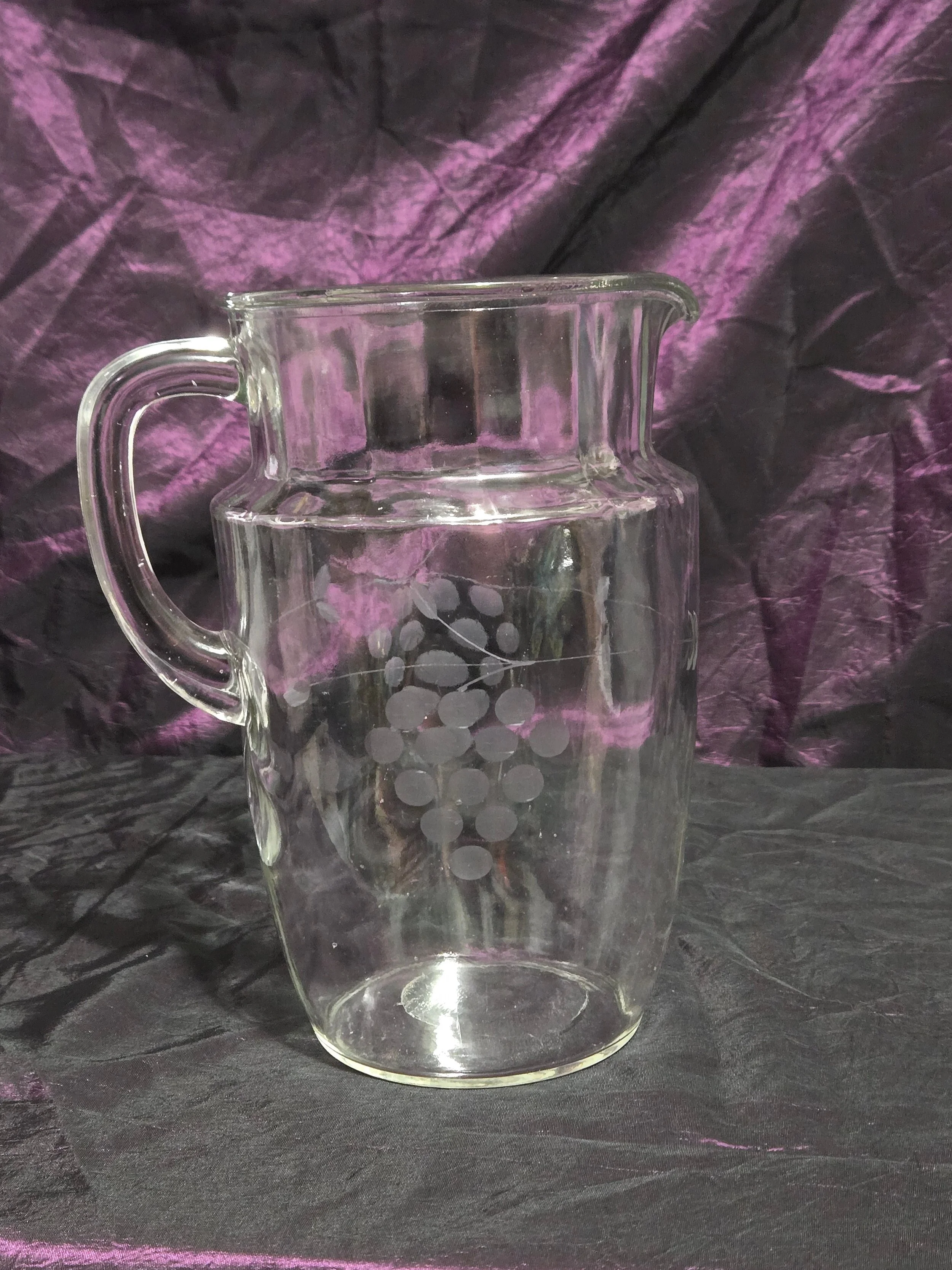 Clear glass pitcher etched with grapevine and crown designs, vintage mid-century style with curved handle and flared spout.