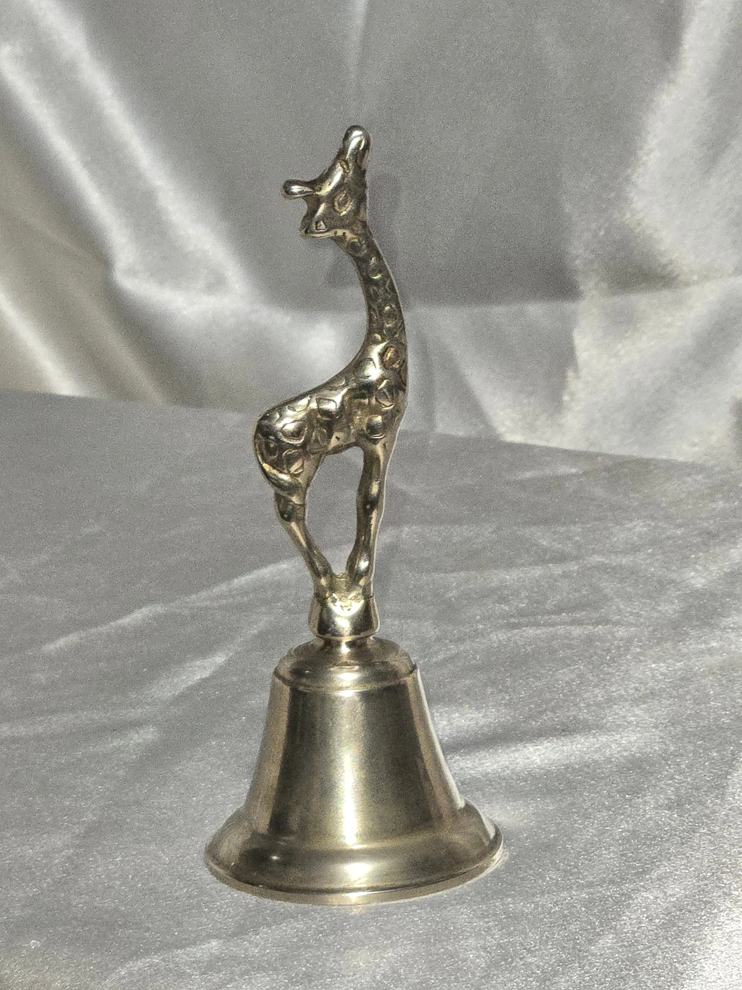 Close-up of vintage brass giraffe-shaped bell standing on silver background, 6 in tall mid-century safari collectible.