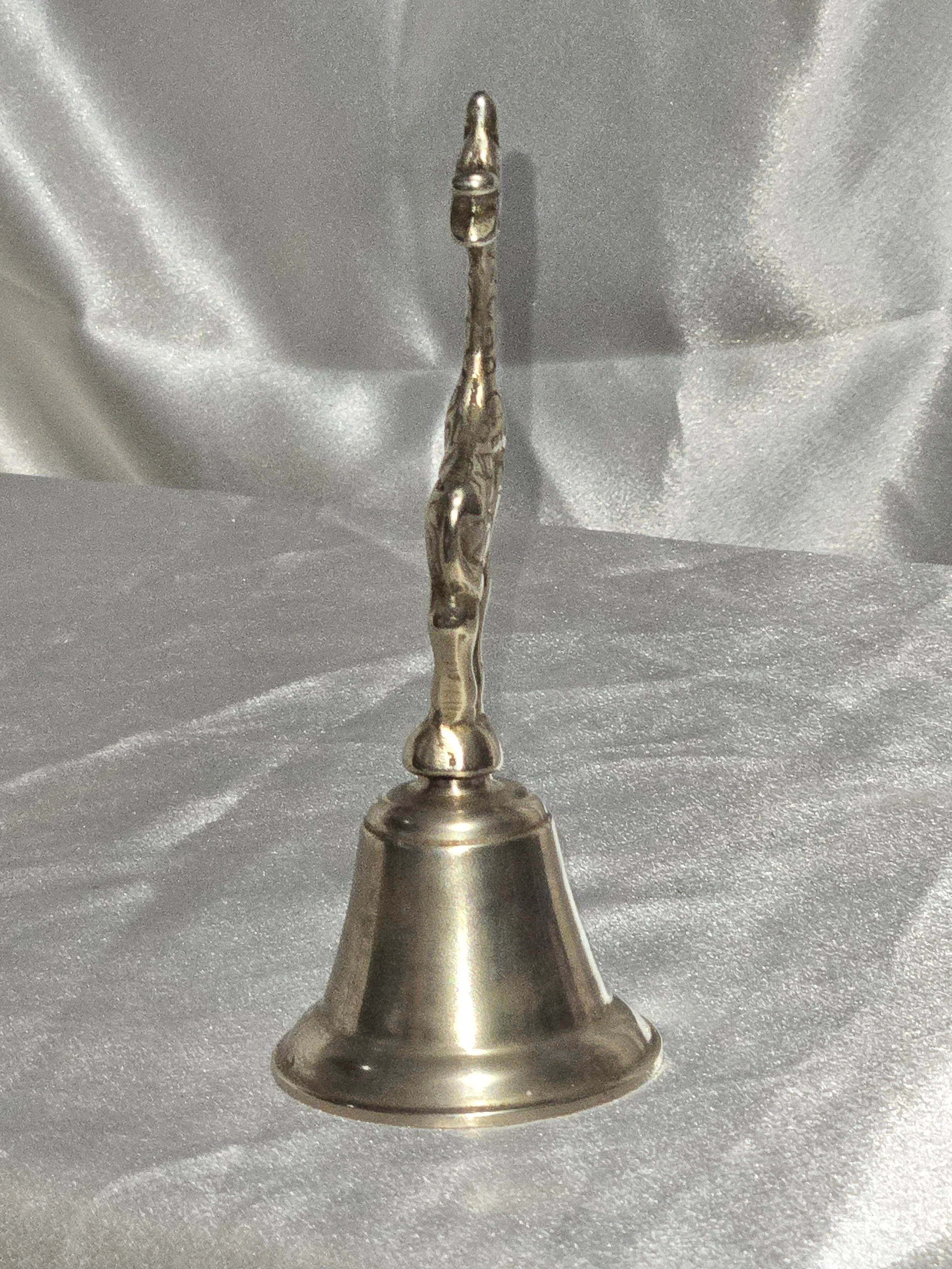 Close-up of vintage brass giraffe-shaped bell standing on silver background, 6 in tall mid-century safari collectible. Rear facing side view