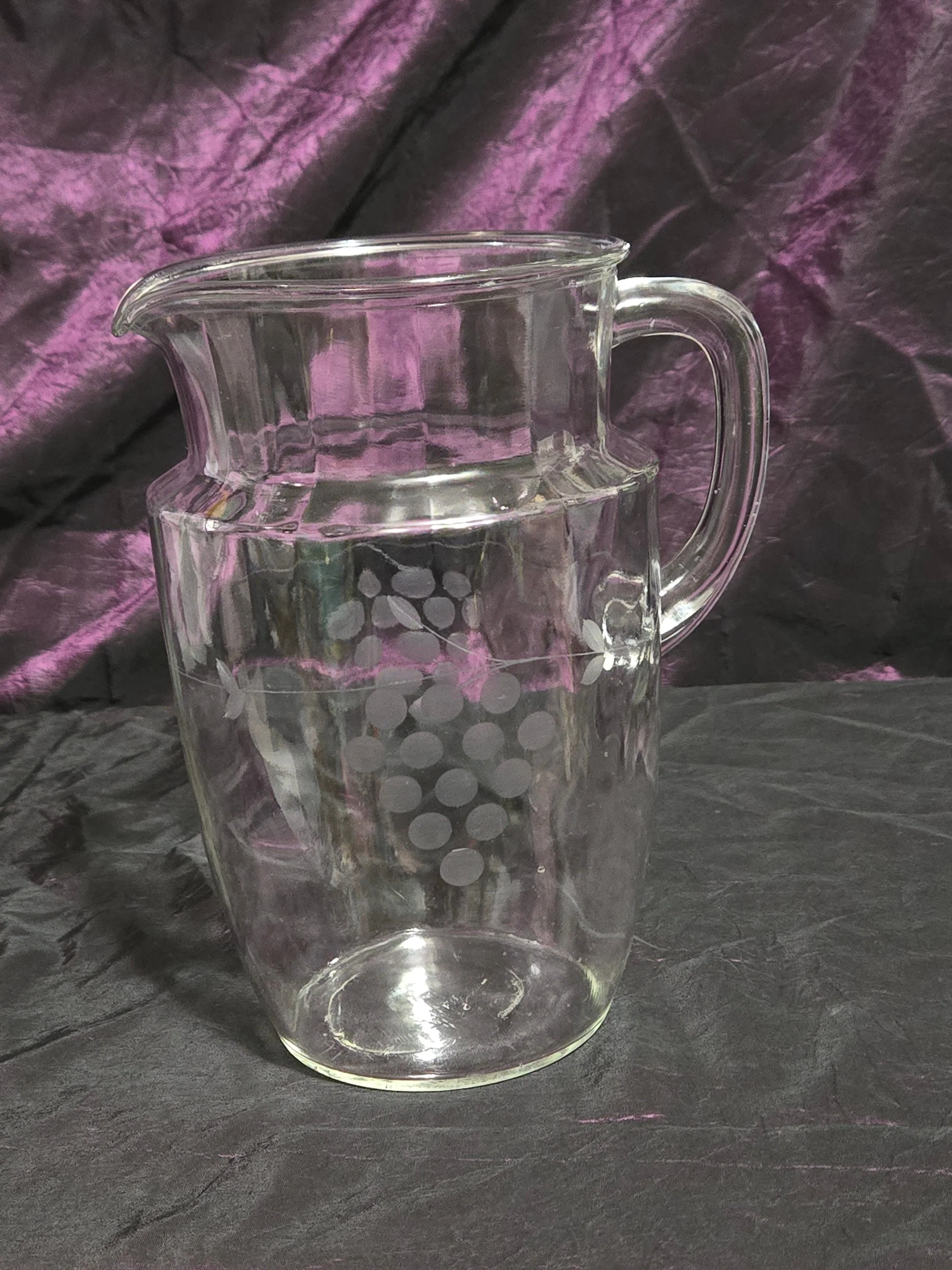 Clear glass pitcher etched with grapevine and crown designs, vintage mid-century style with curved handle and flared spout.