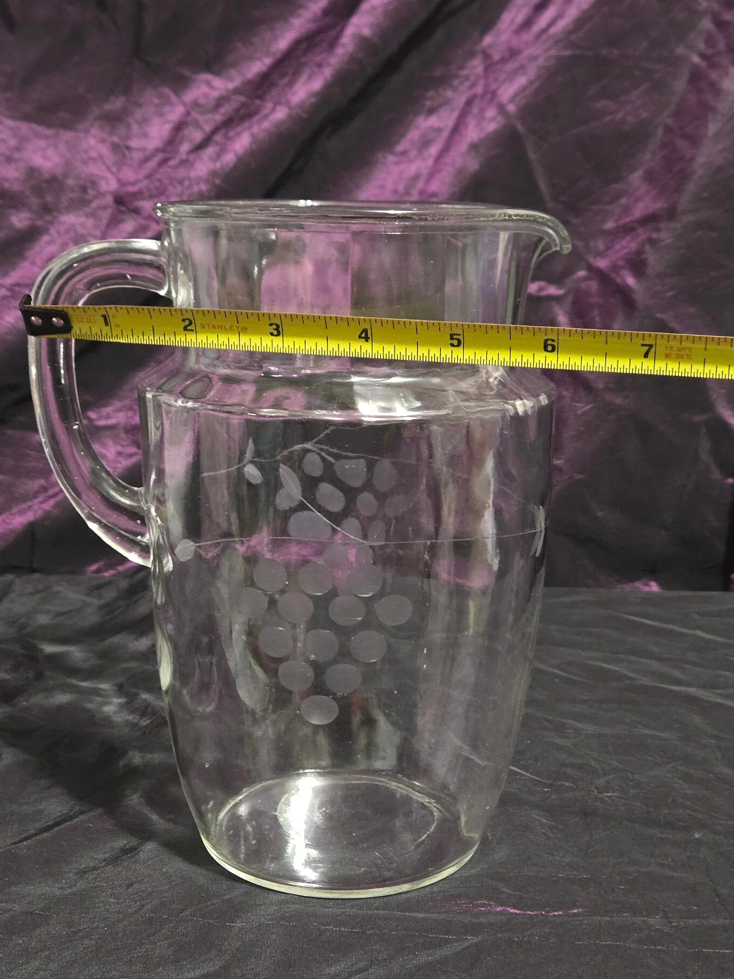 Clear glass pitcher etched with grapevine and crown designs, vintage mid-century style with curved handle and flared spout.