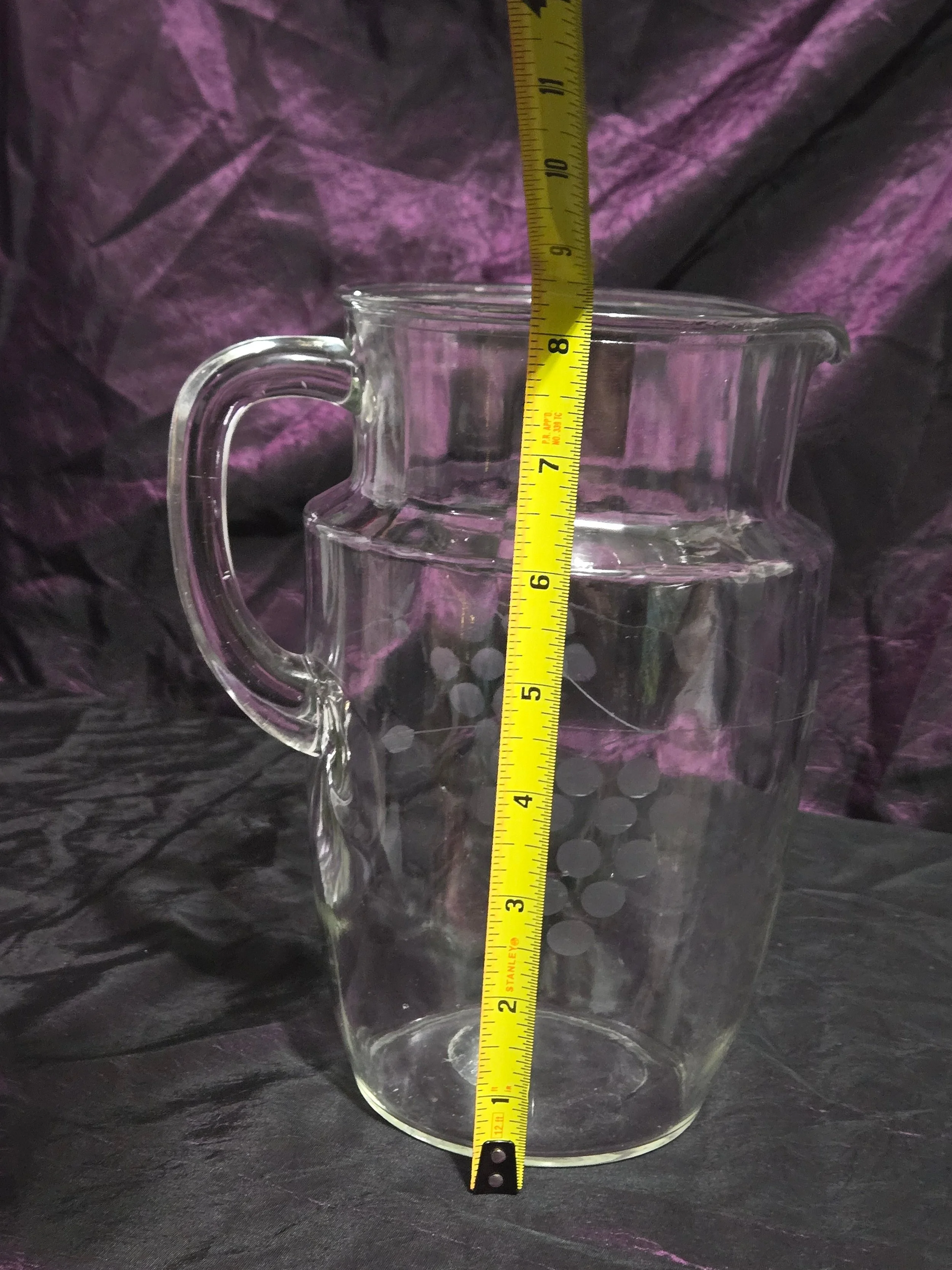 Clear glass pitcher etched with grapevine and crown designs, vintage mid-century style with curved handle and flared spout.